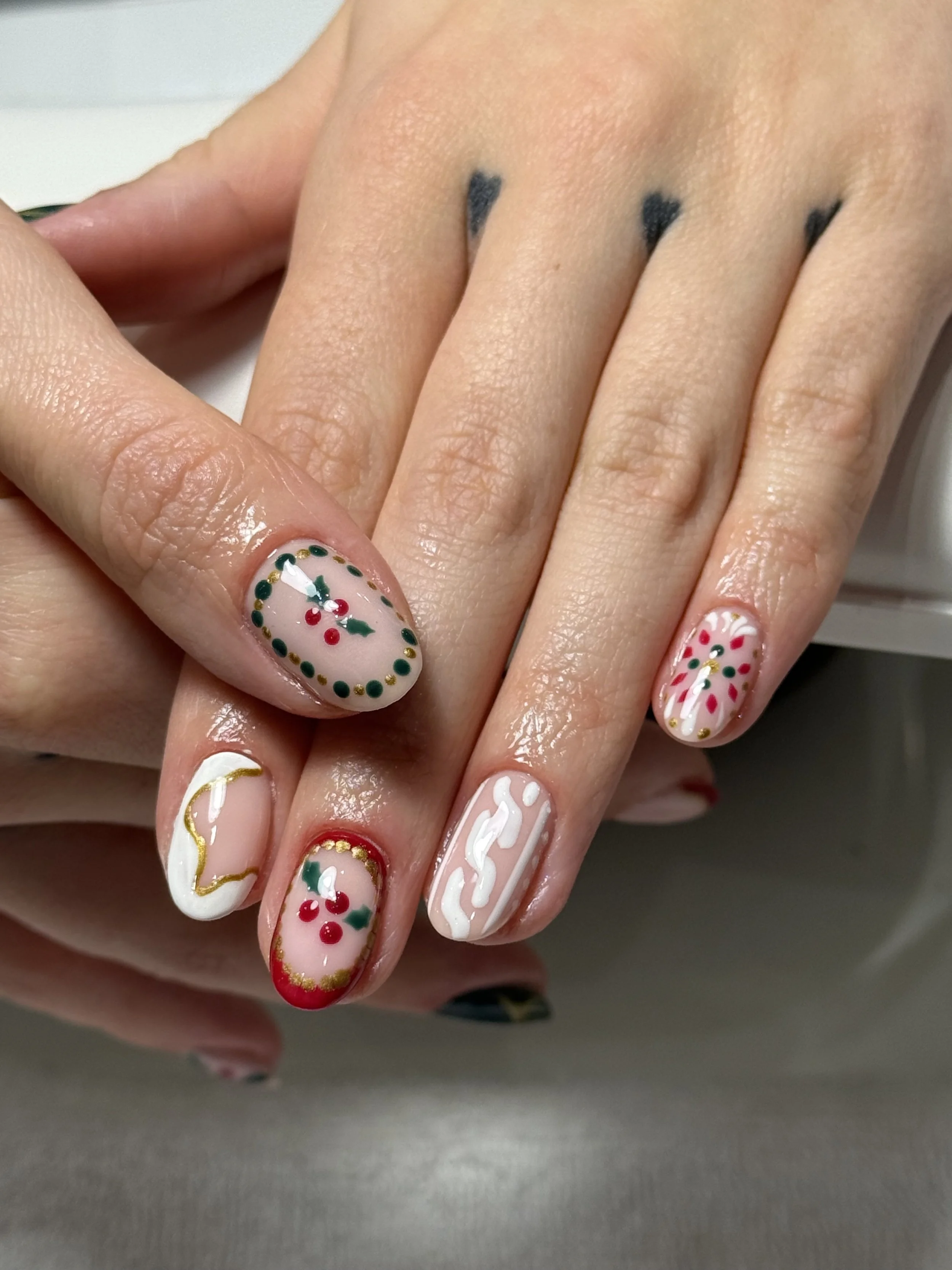 Close-up of a hand with decorated Christmas-themed nails, including designs of holly, berries, wavy gold lines, and red tips.