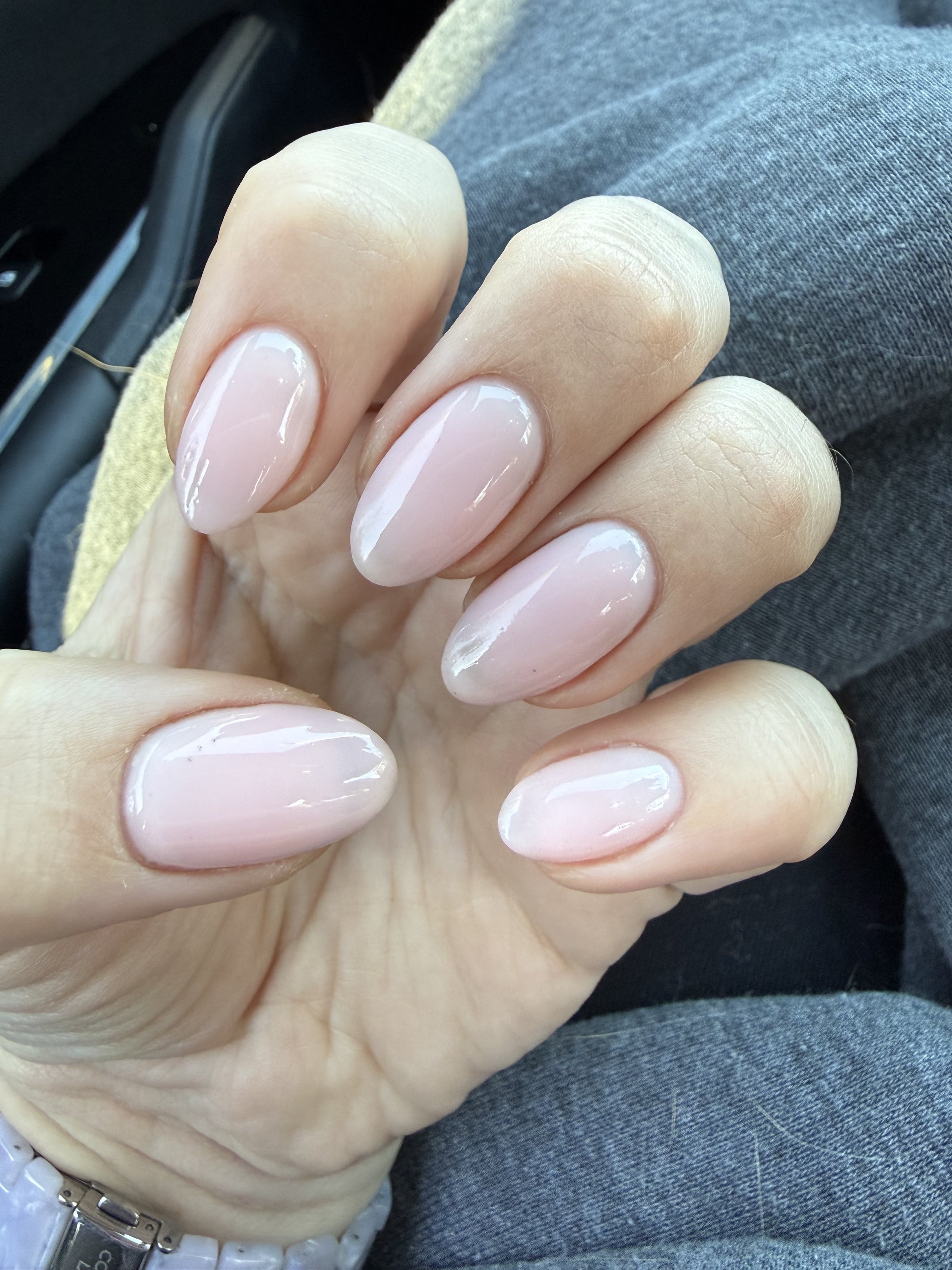 Close-up of a person's hand showing nails with a natural, shiny, light pink manicure.