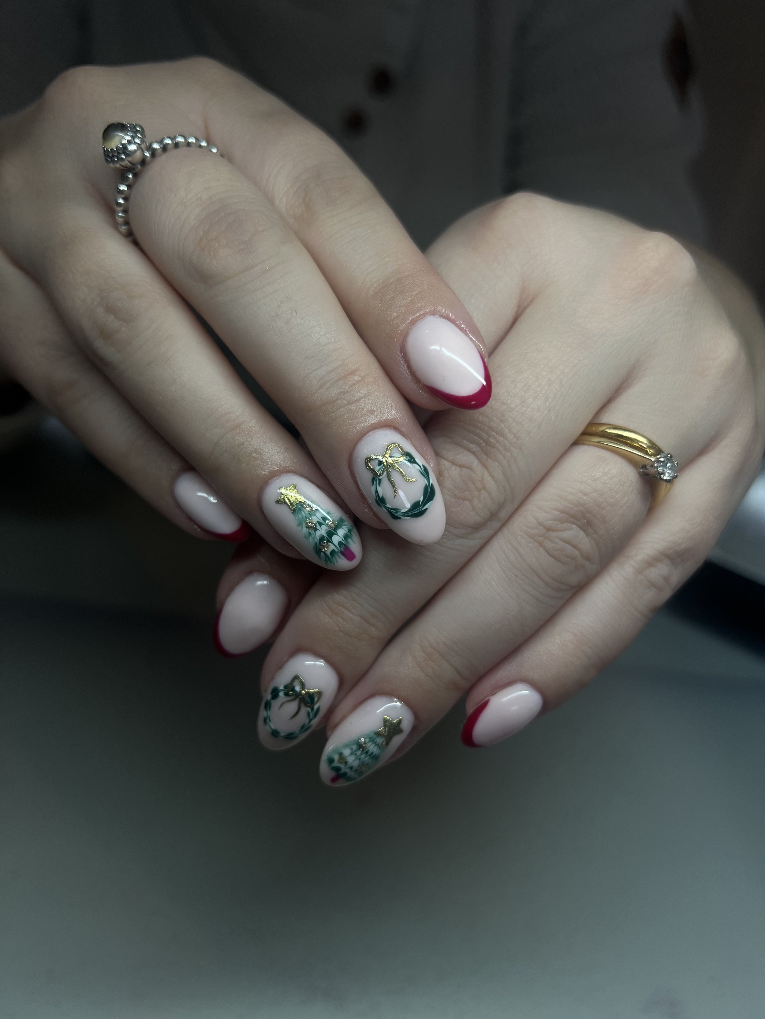 Person with holiday-themed nail art and multiple rings on fingers, including a silver ball ring and a gold ring with a diamond
