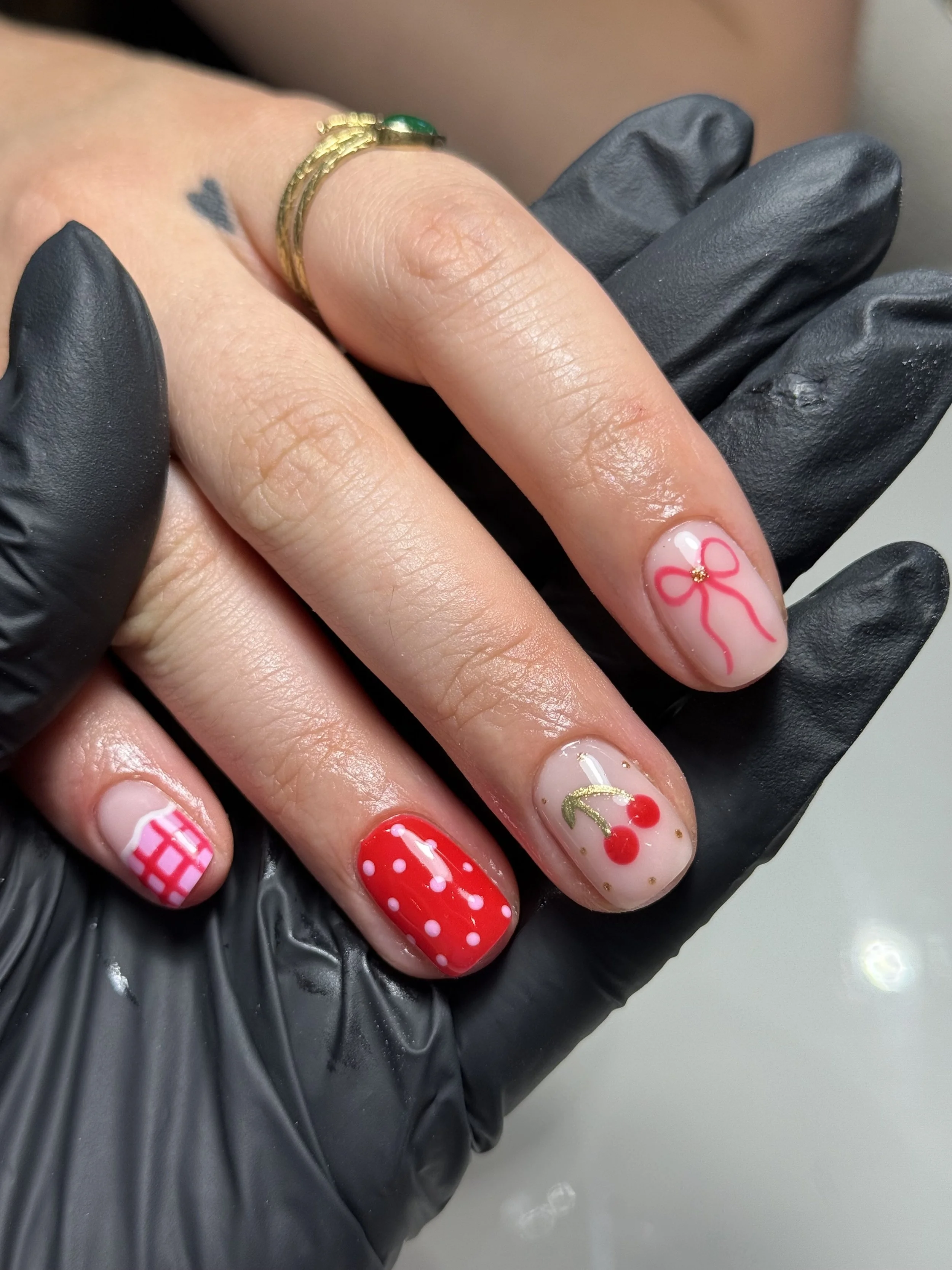 Close-up of a hand with decorated nails and wearing a gold ring, held by a gloved hand.