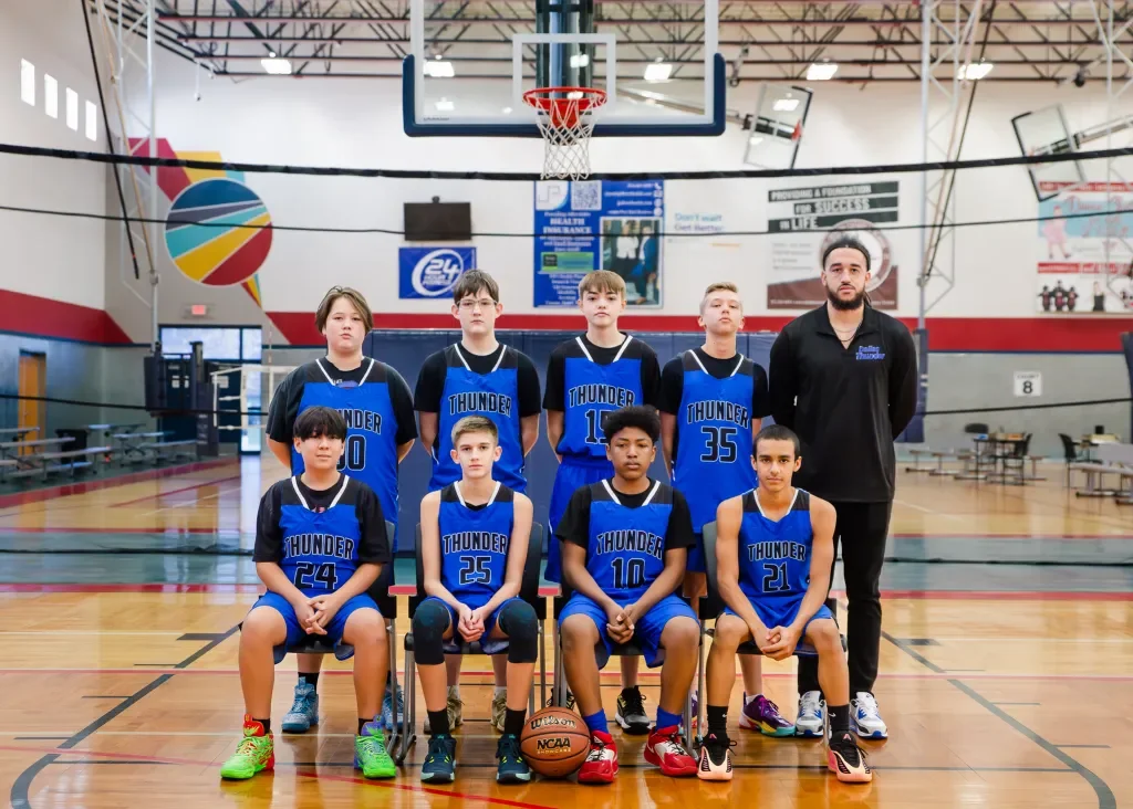Youth basketball team in blue jerseys with 'Thunder' written on them, posing with coach in an indoor gymnasium.