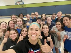 Group of young women and girls smiling and giving thumbs up in a gymnasium.