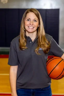 A woman with long red hair holding a basketball, standing on a basketball court.