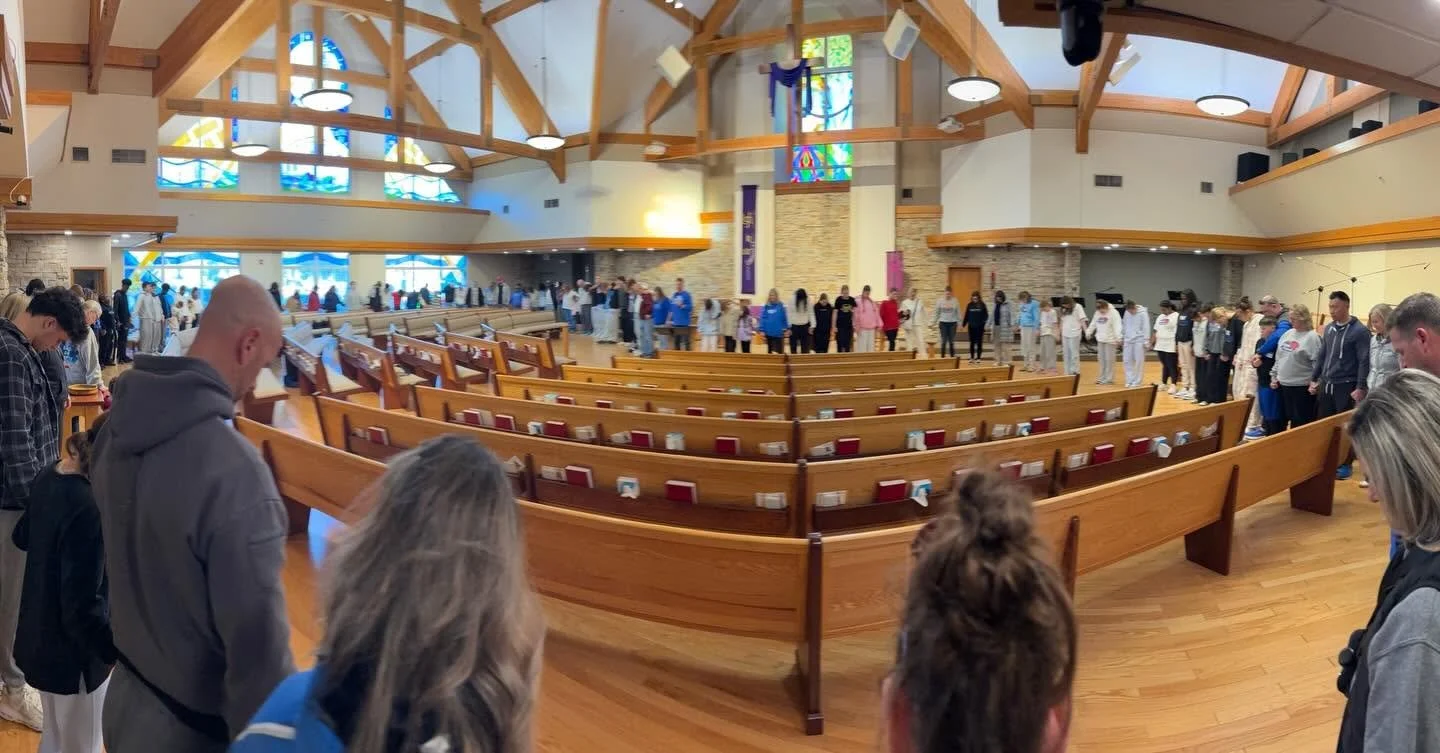 People praying inside a church with wooden pews and stained glass windows.