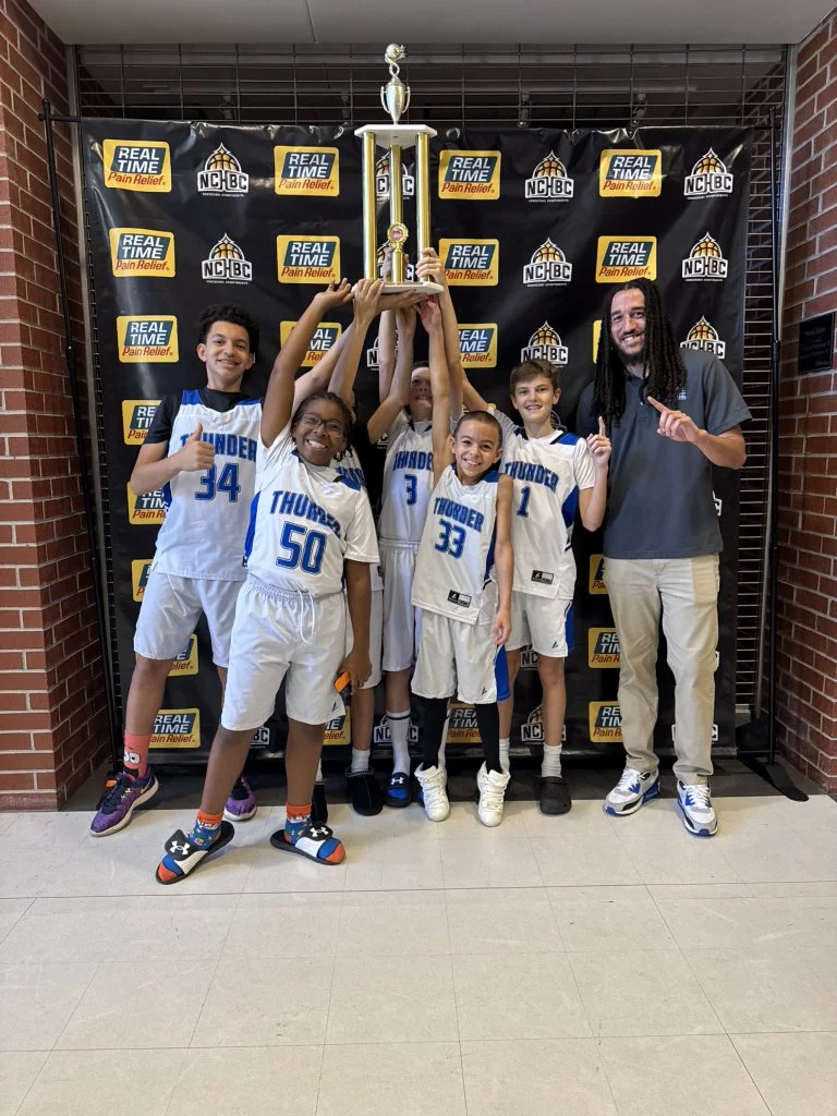 A youth basketball team called the Thunder celebrating with a coach or parent, holding up a trophy after a victory.