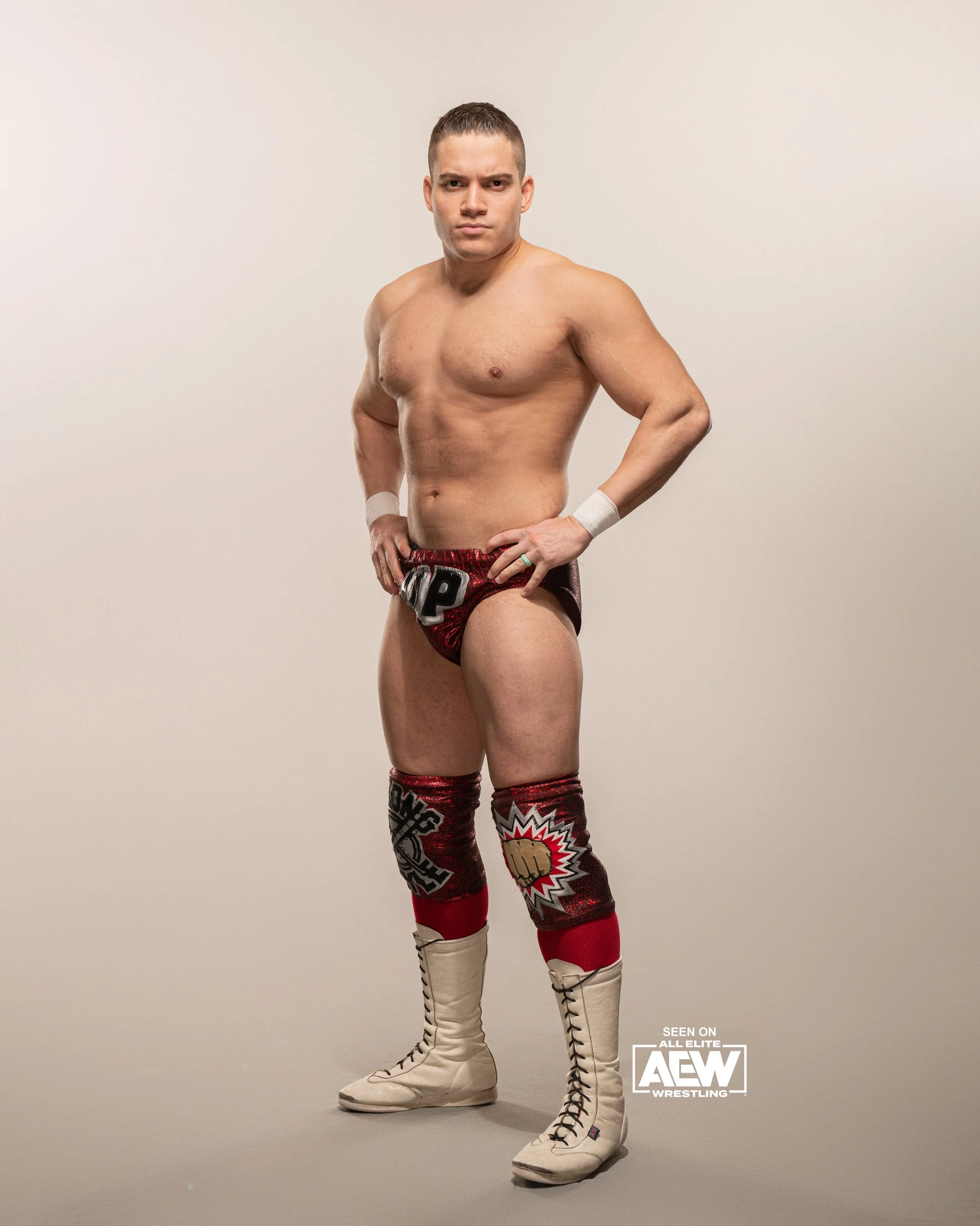 Professional wrestler standing confidently in wrestling trunks and boots, against a plain background.