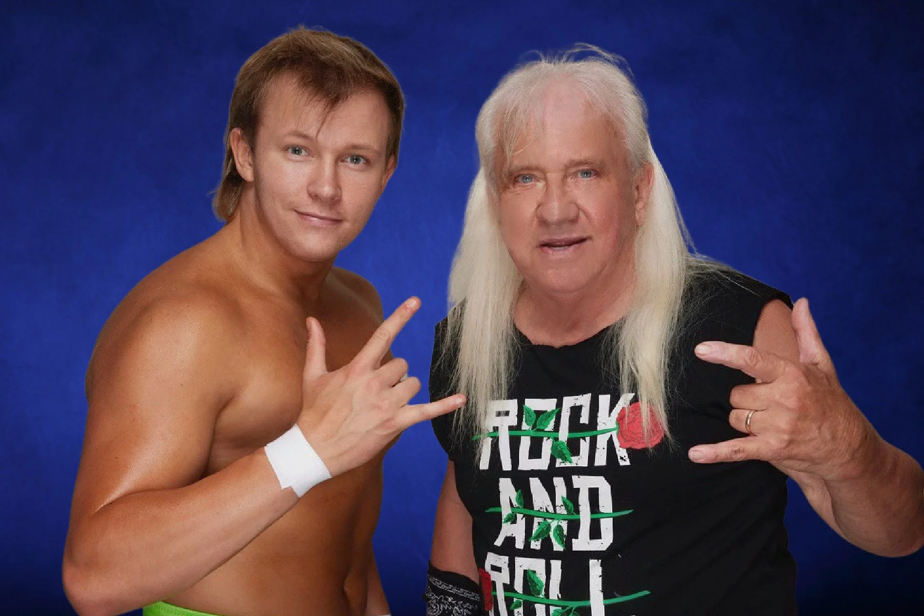 A shirtless young man with brown hair and a white wristband making a wrestling hand sign, standing next to an older man with long white hair, wearing a black T-shirt with colorful text, both making rock and roll hand signs against a blue background.
