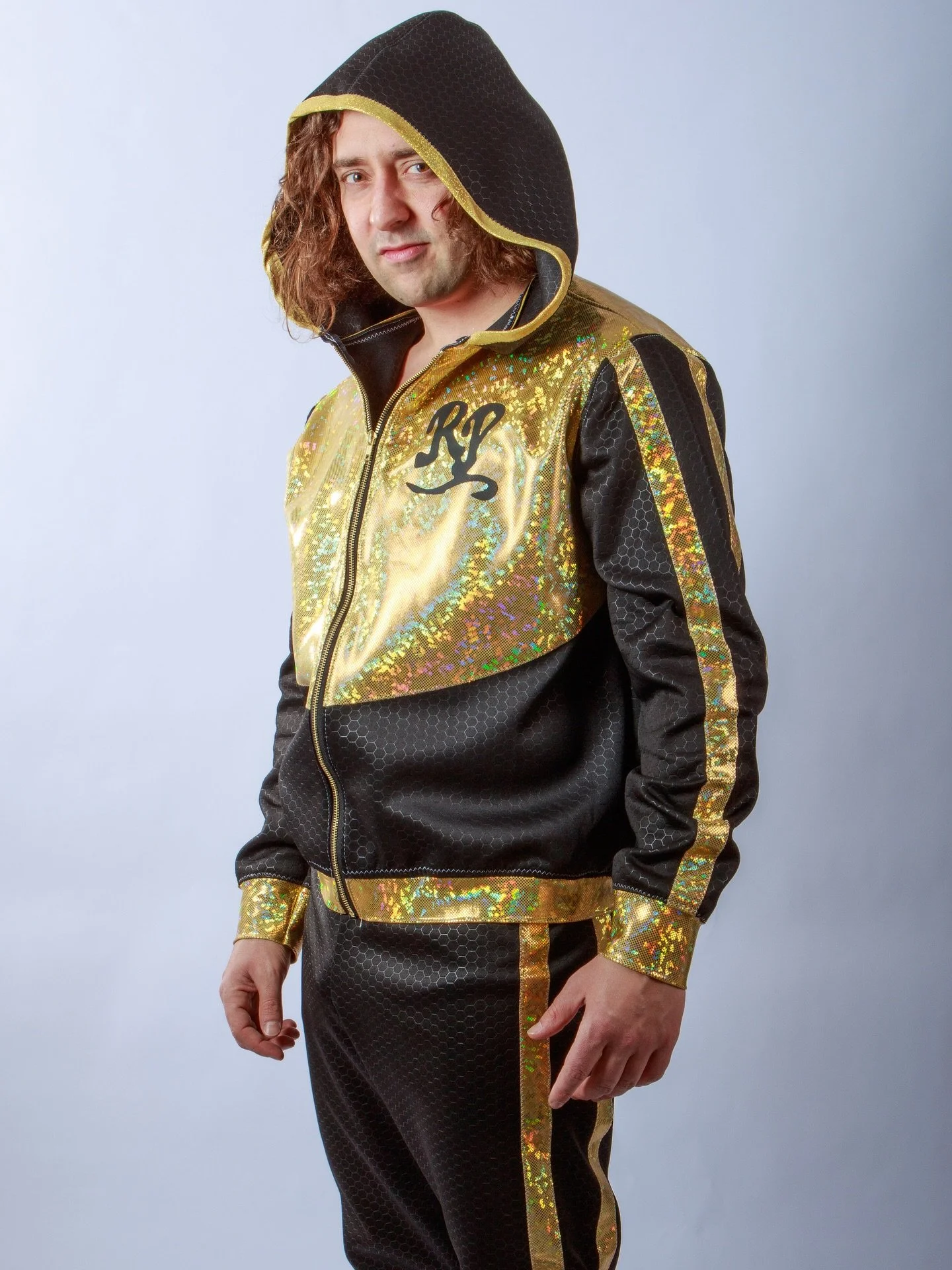 Person wearing a black and gold holographic tracksuit with a hood, standing against a plain gray background.