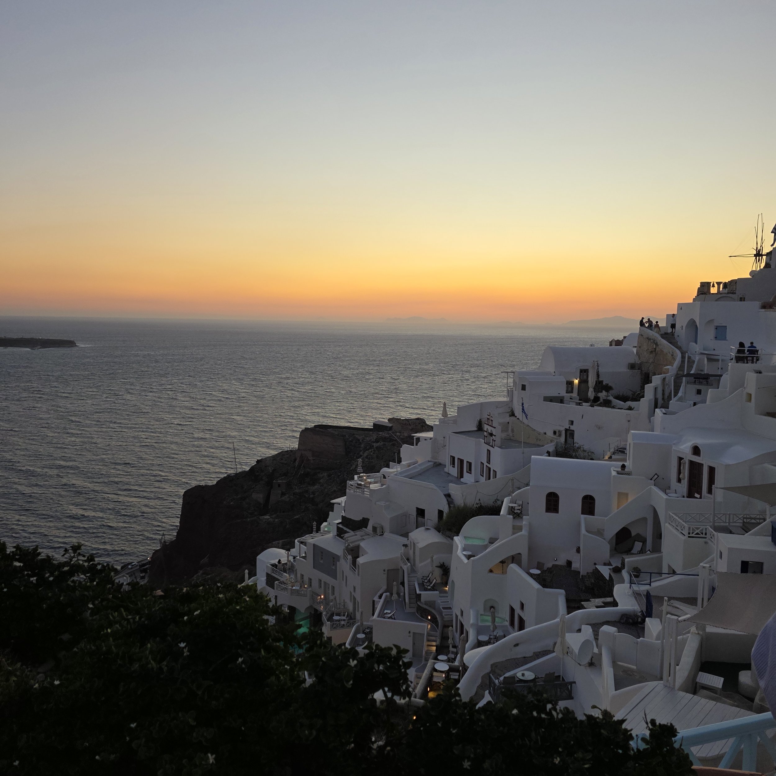 Caldera sunset view in Oia, Santorini, with white buildings overlooking the sea.