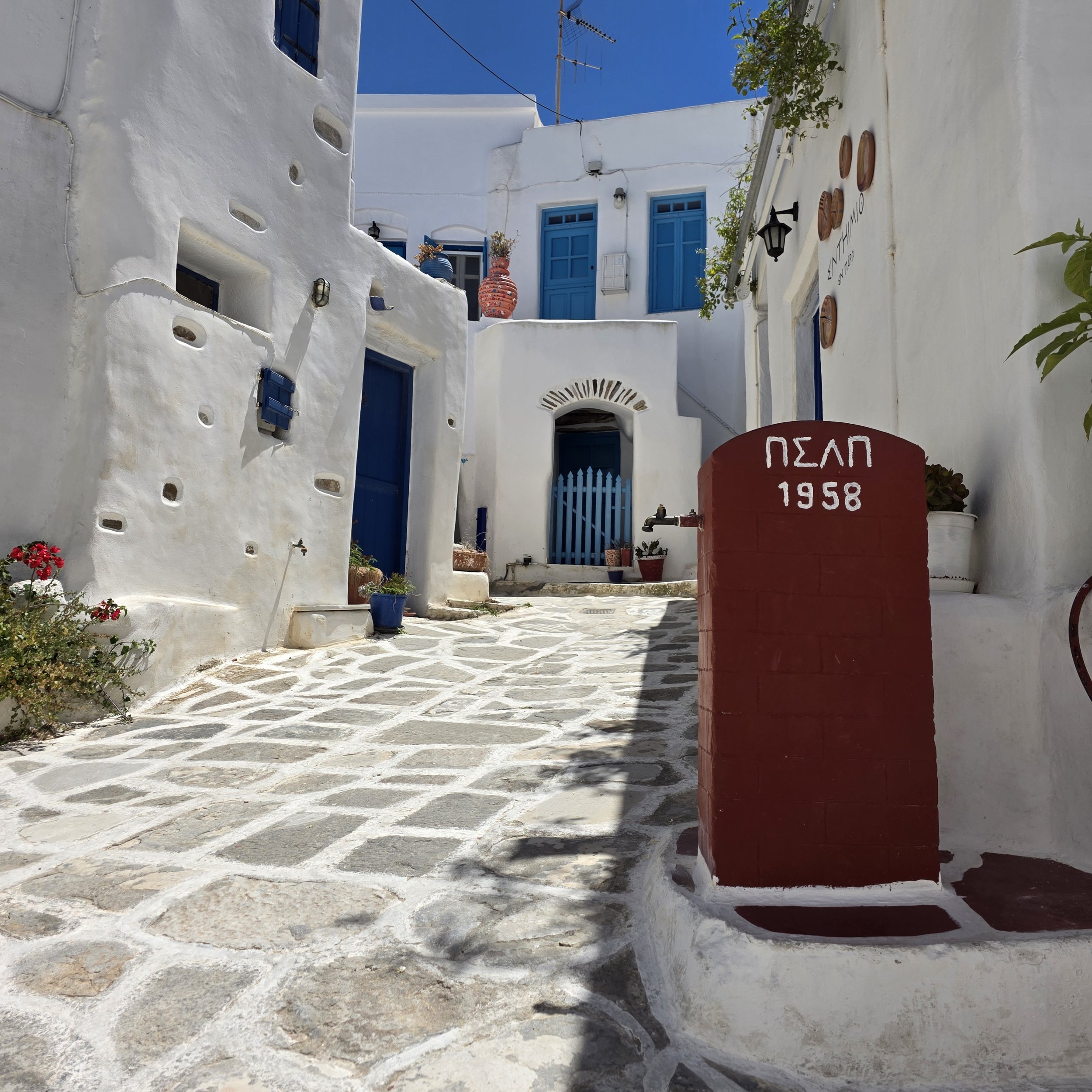 Narrow whitewashed street in the hilltop village of Lefkes, Paros, Greece, with blue doors and stone pathways.