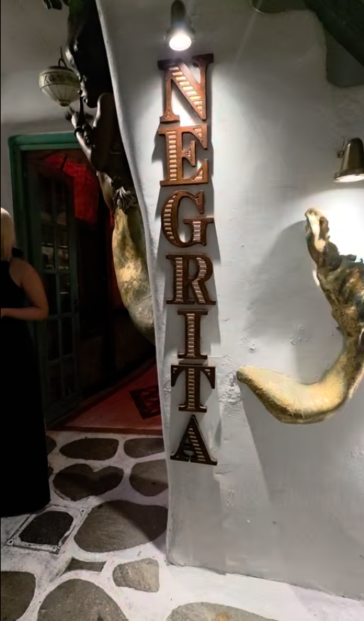 Negrita Bar entrance in Mykonos, Greece, with a decorative sign and sculptural wall art.