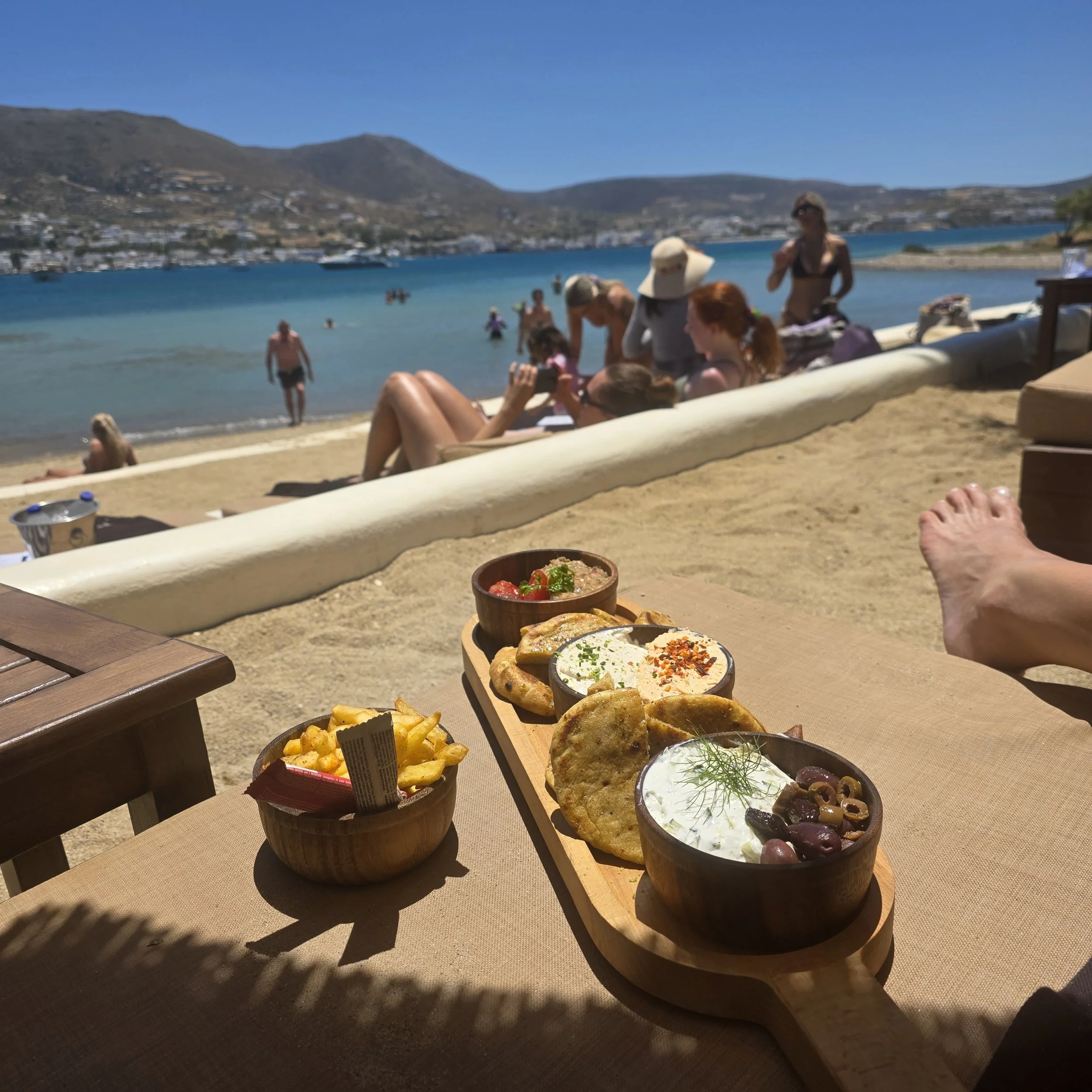 Greek meze spread with tzatziki, fries, and pita at Cabana Beach Club on Paros, Greece, with the beach in the background.