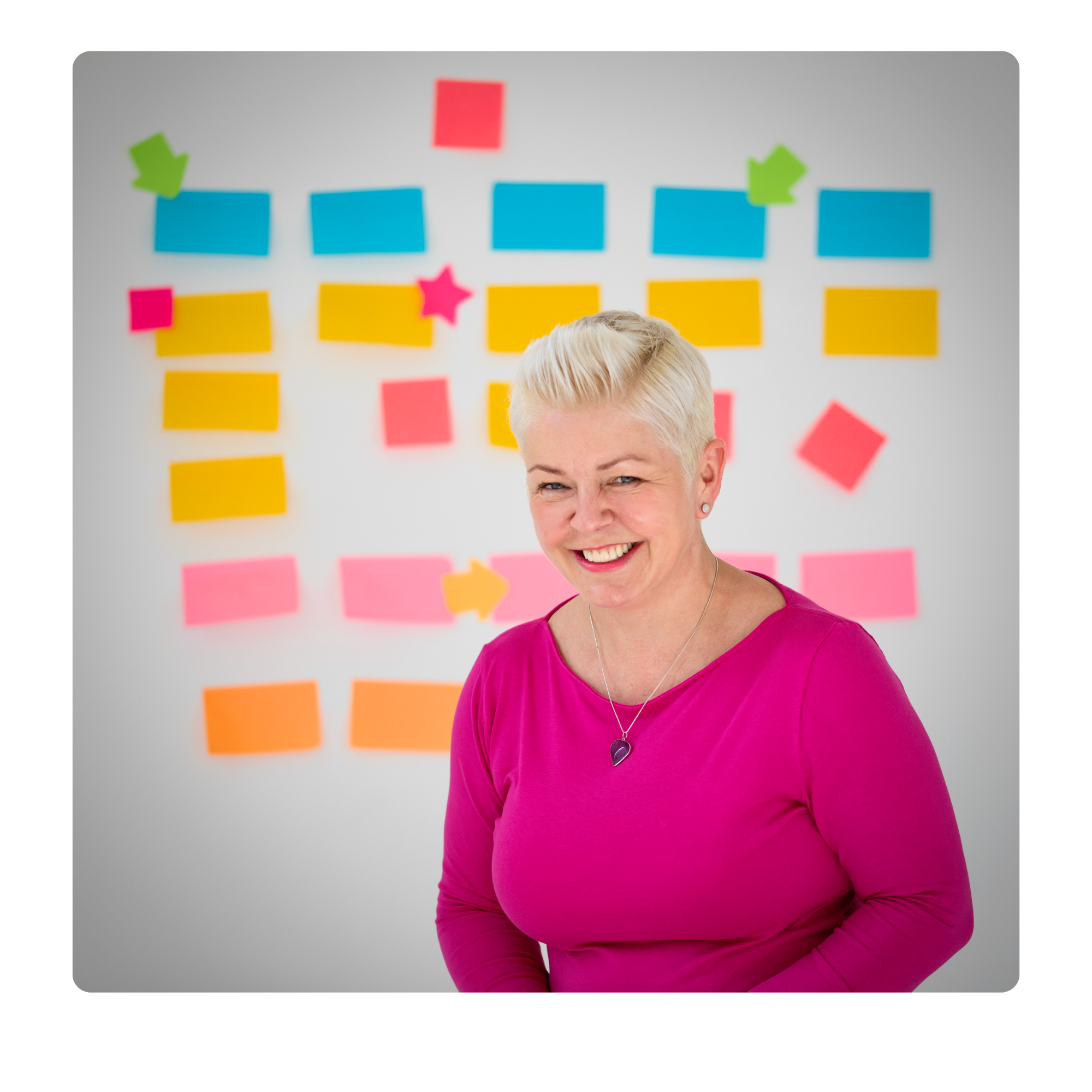Jenny Martin, wearing a pink top in front of a wall covered with colourful sticky notes.