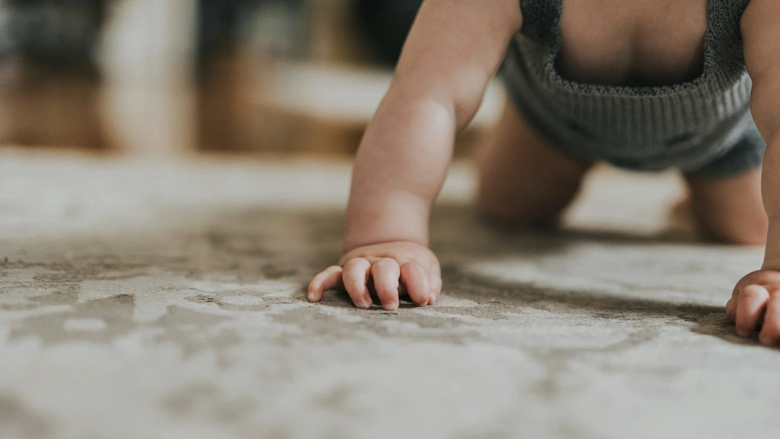 Close-up of a baby crawling on a carpeted floor, supporting themselves with one hand and one knee.