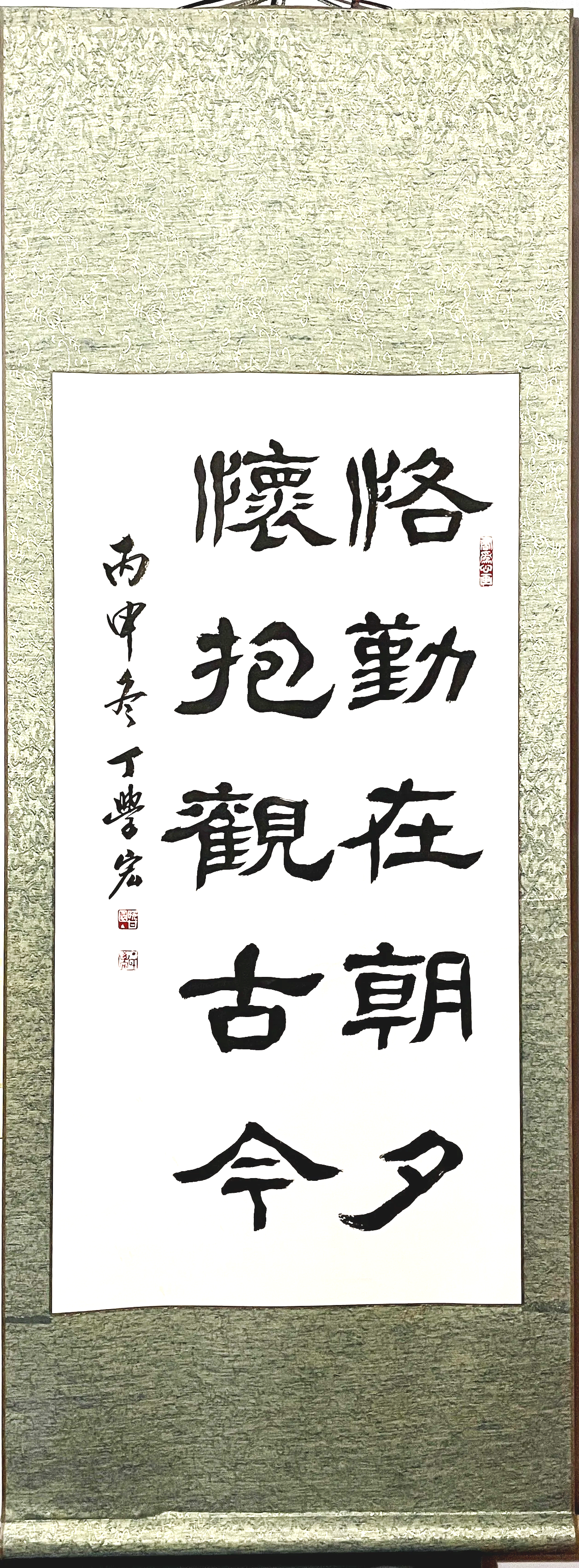 Traditional Chinese calligraphy scroll with black characters on white background, framed with decorative greenish-gold border.