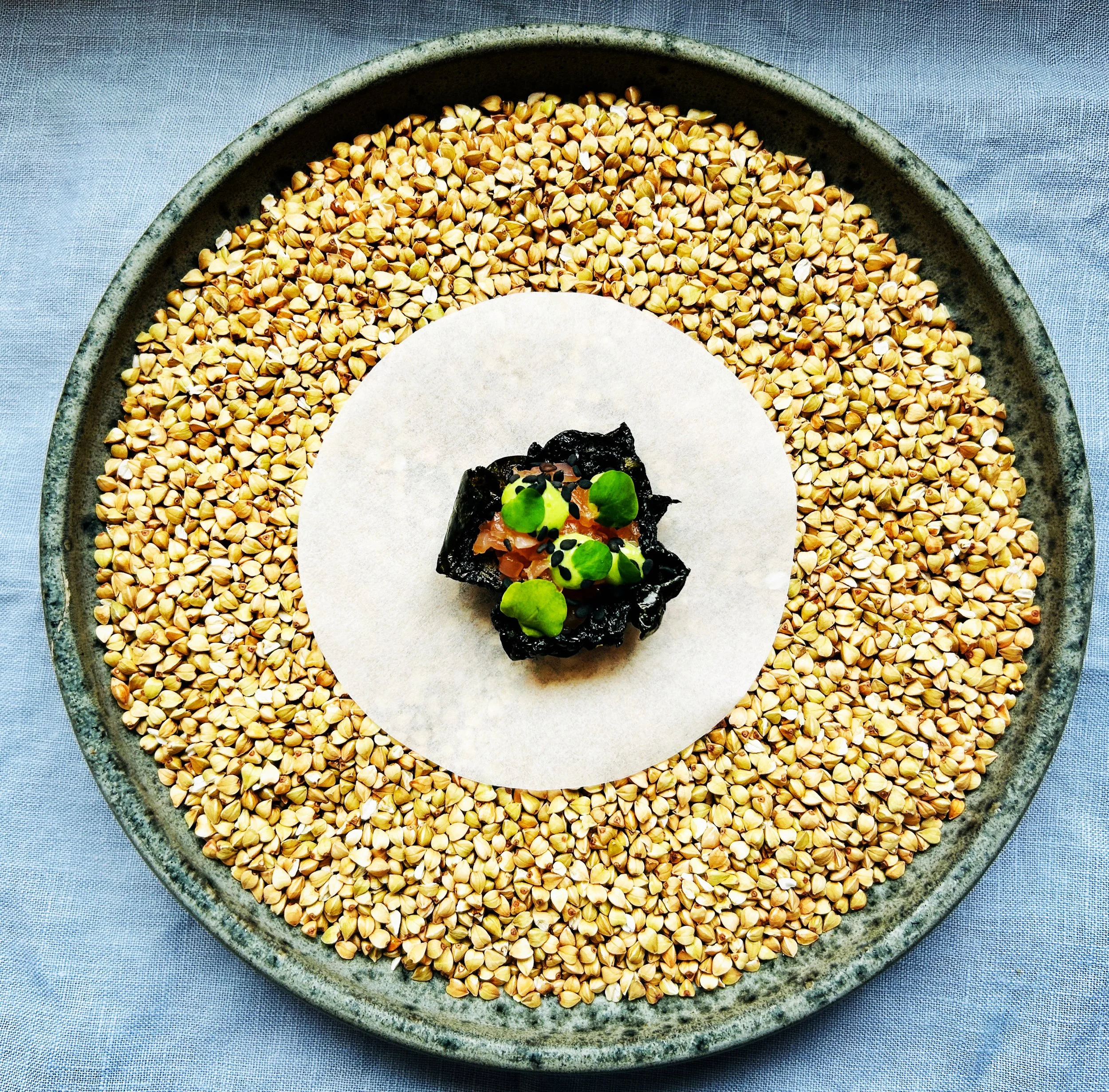 A round platter filled with buckwheat grains on a gray cloth background.