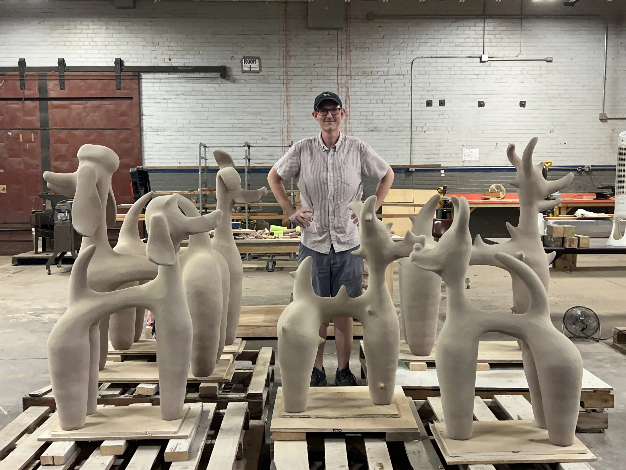 Ryan Osborne standing next to his recently finished large scale dog sculptures prior to firing.