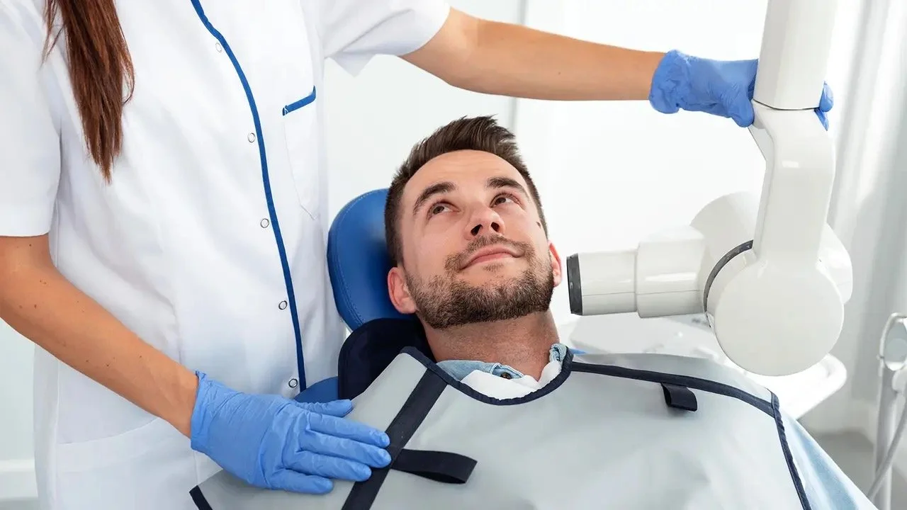 A man lying in a dental chair with a doctor using a dental microscope for examination.