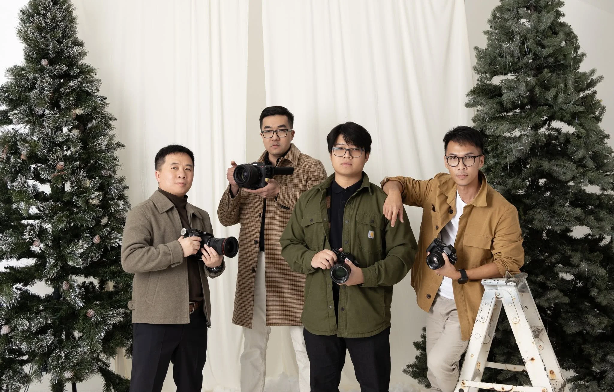 Group of five men holding cameras posing in front of Christmas trees and white curtains.