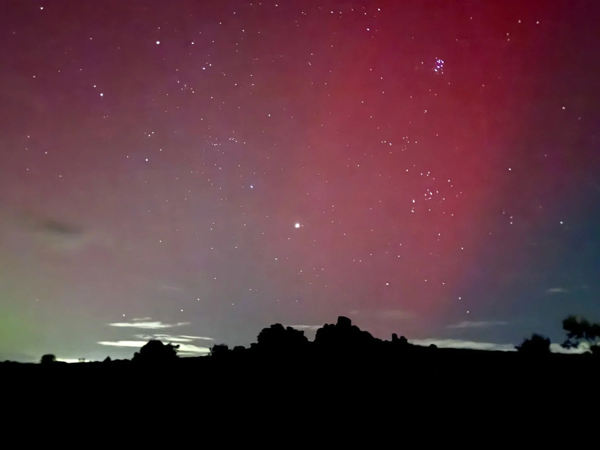Nighttime landscape with stars and a radar dish silhouette, colored by aurora borealis.