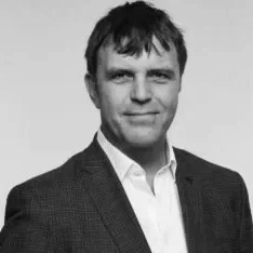 Black and white photo of a man in a suit with short dark hair, smiling slightly at the camera.