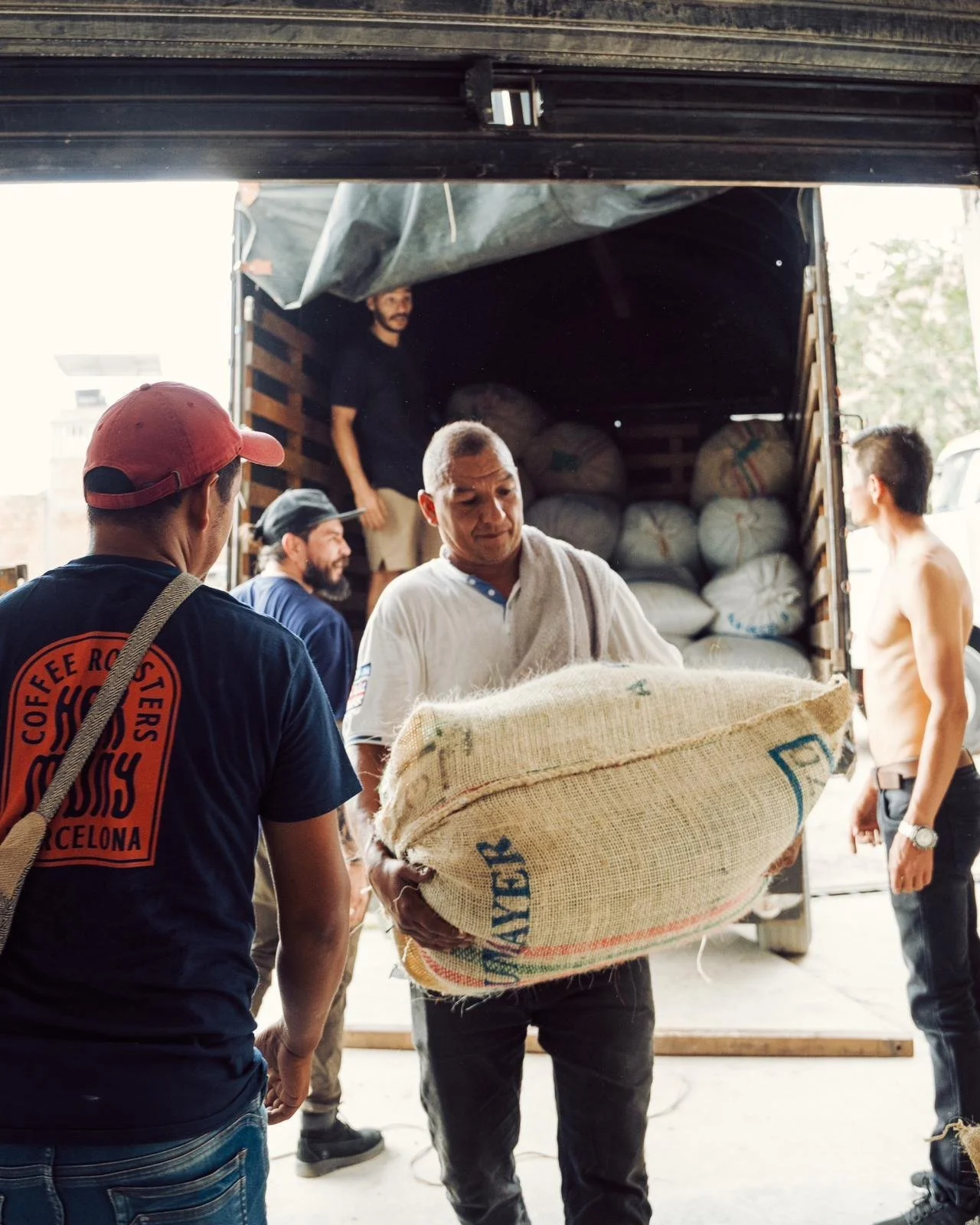 Prepping for high quality green coffee imports carrying a burlap sack of coffee off of a truck at origin in Colombia
