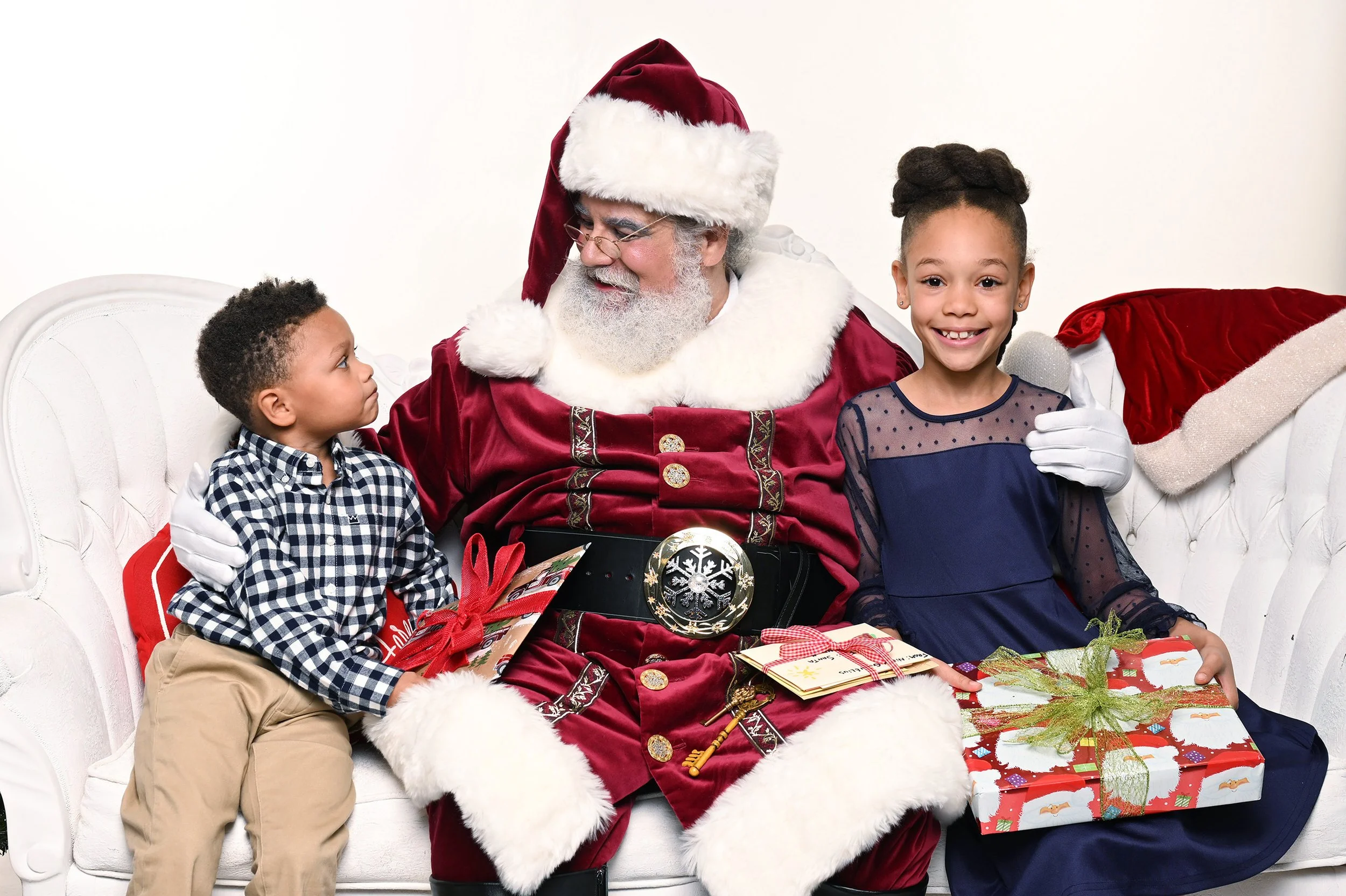 A young boy sits to Santa's right and looks up at him, while a teen girl is on Santa's left and smiles broadly.