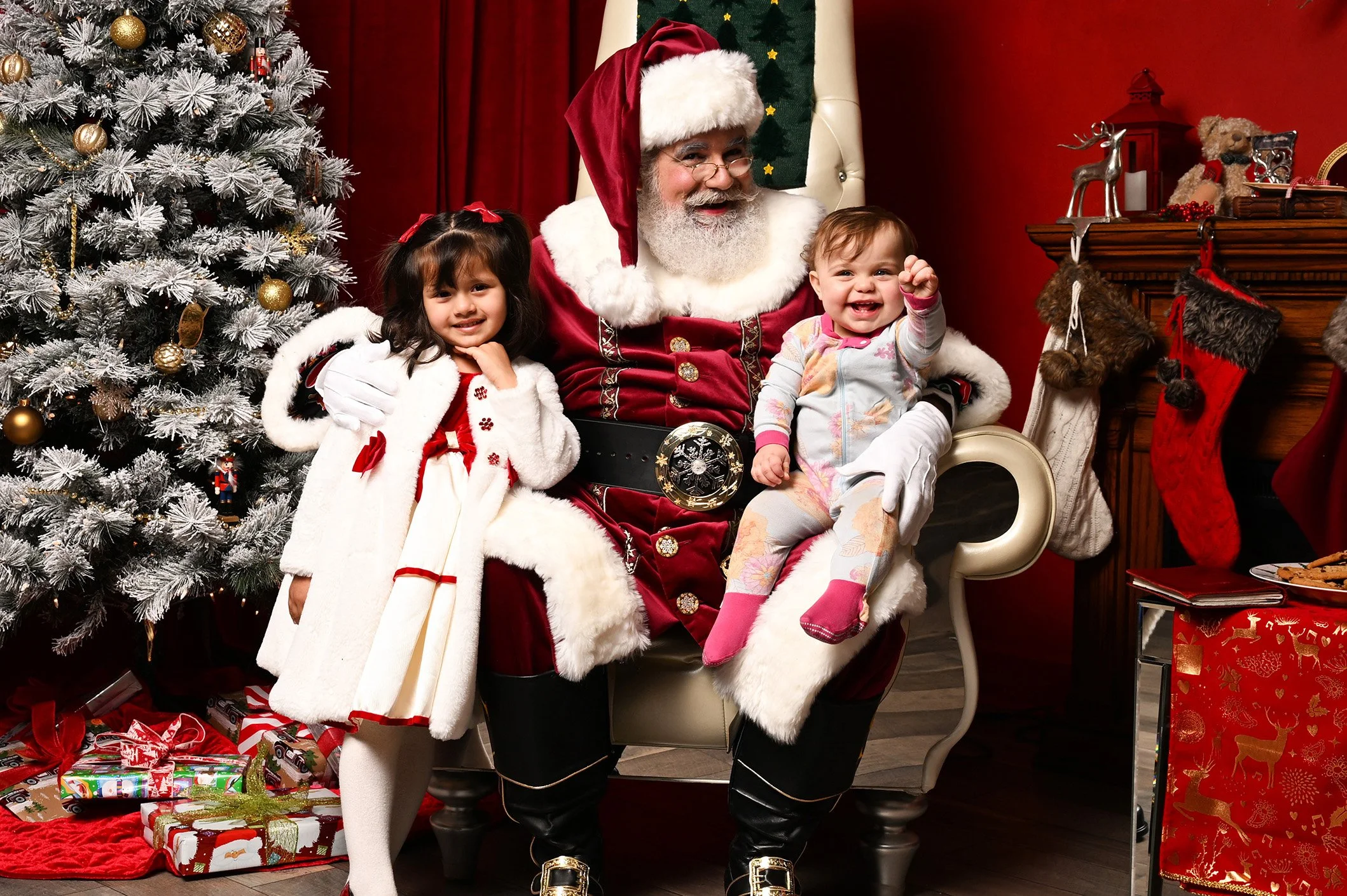 A happy girl and a toddler sit with Santa Claus.
