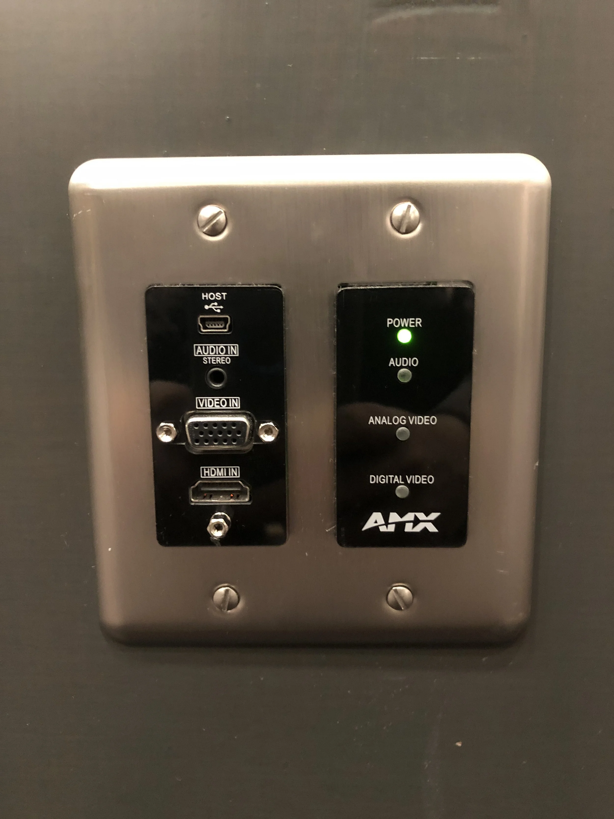 Close-up of an audio-visual control panel with various input options, including HDMI, VGA, and audio connectors, mounted on a metallic surface.