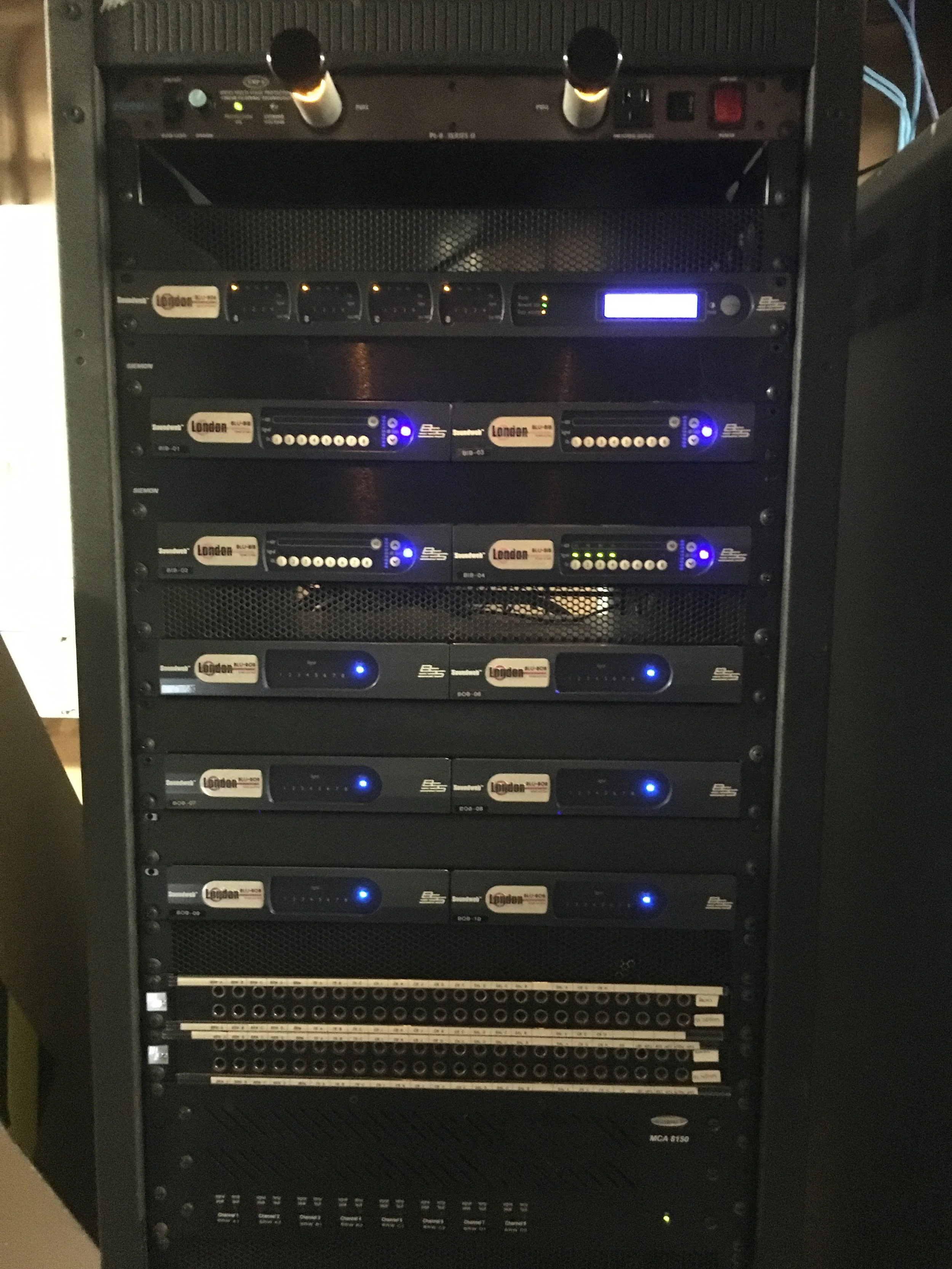 A black server rack containing multiple audio and electronic equipment units with various lights, switches, and ports.