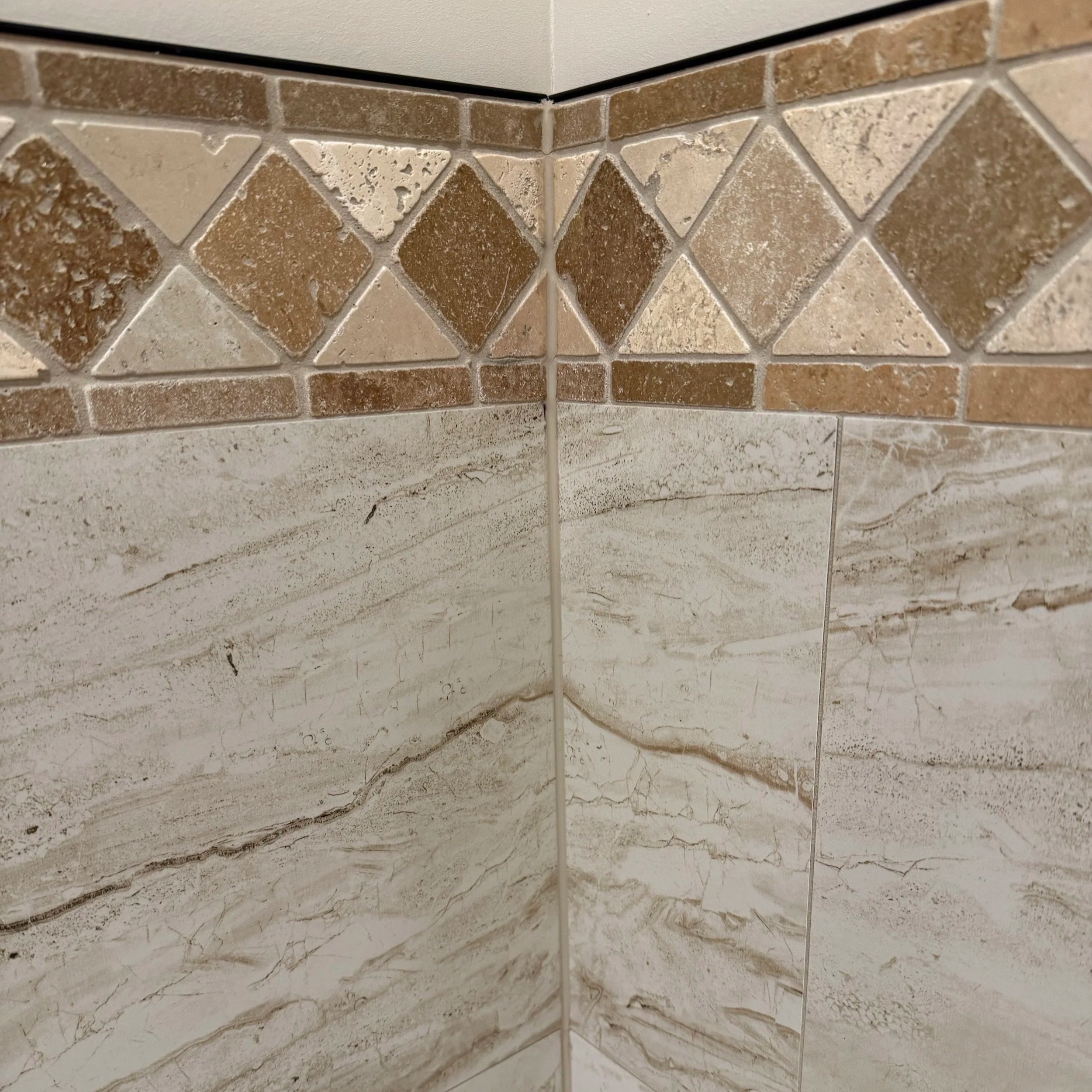 Close-up view of brown and beige textured tile pattern on a wall, with a corner and white grout lines.