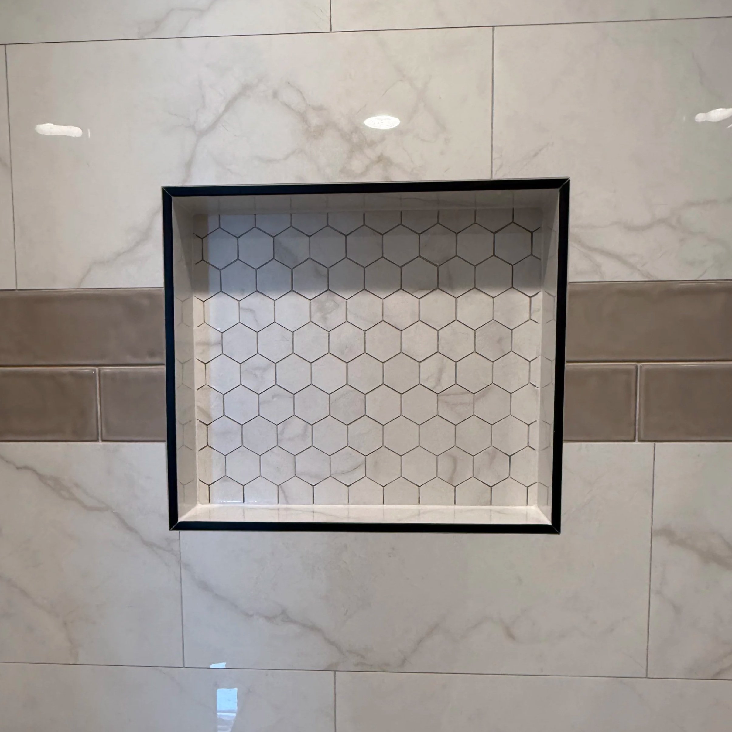 Marble wall with large tiles, a recessed open shelving area with hexagon tiles, and reflection of ceiling lights.