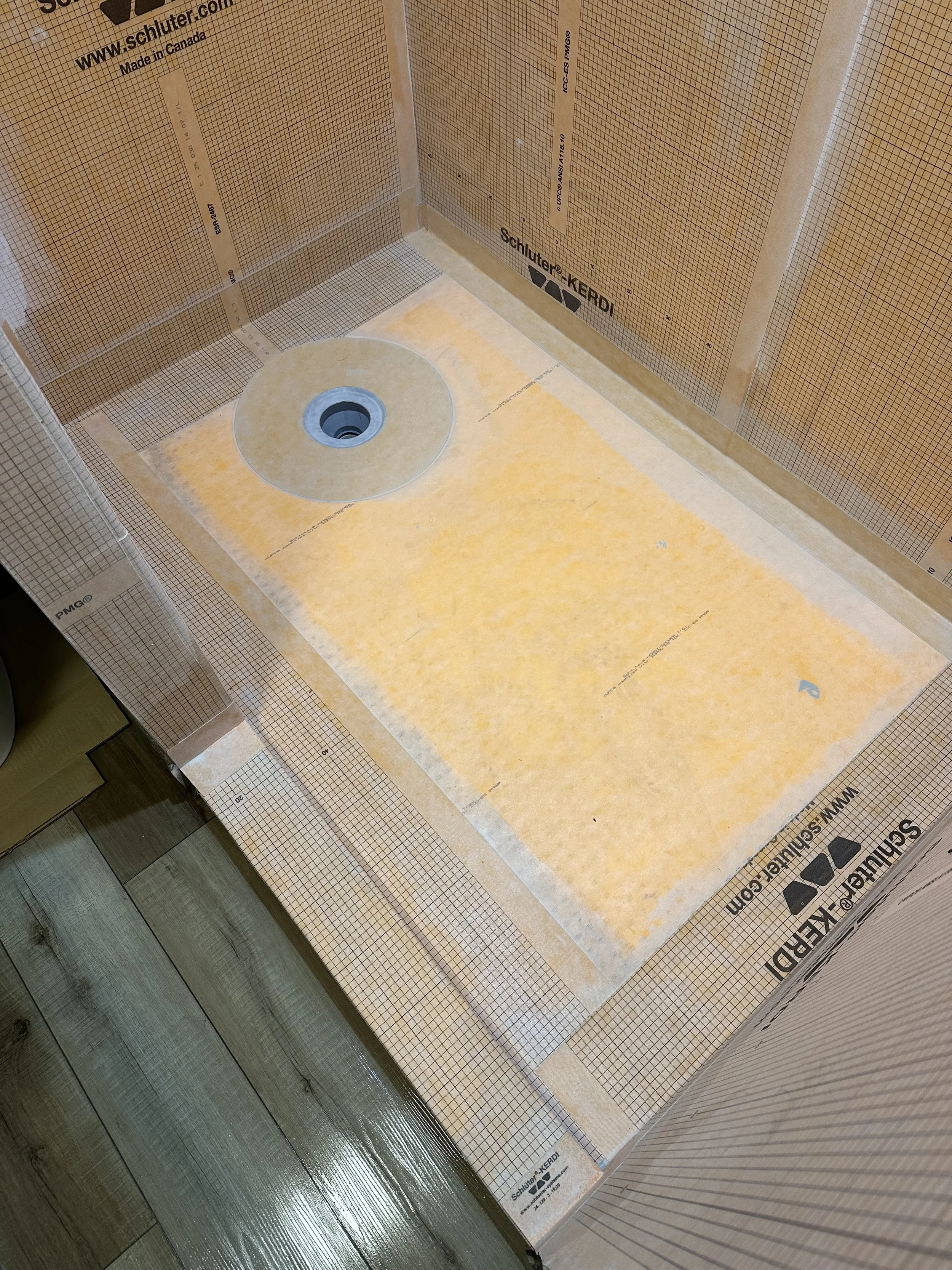 This image shows the inside of a room under construction with drywall panels and a floor drain installed.