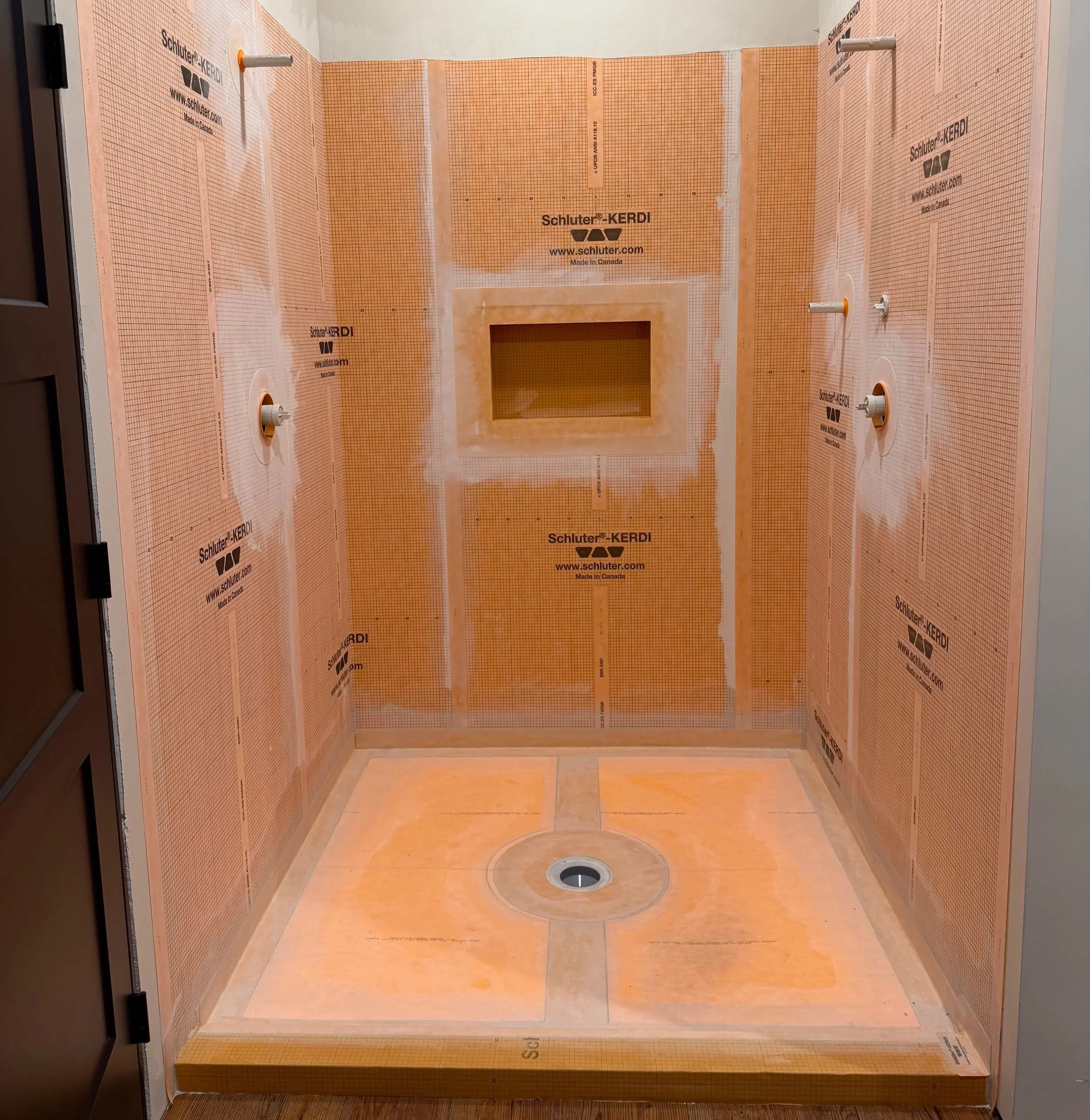 An unfinished bathroom shower area with orange waterproof backer board and a floor drain, framed for tiling installation.