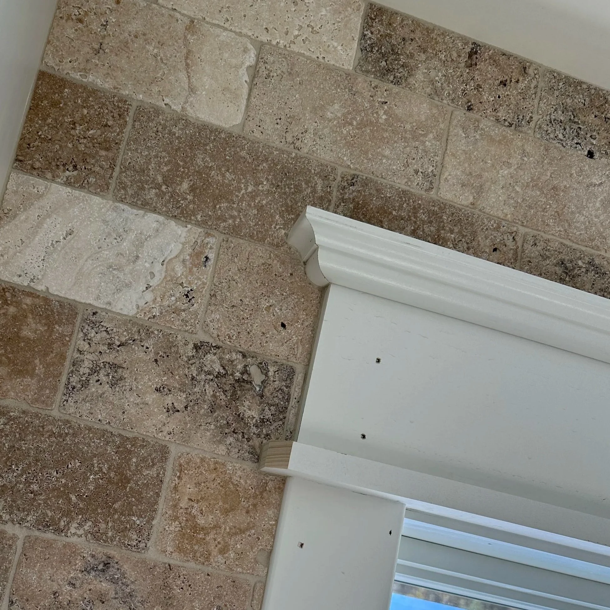 Close-up of a tiled floor with tan, beige, and brown stone tiles and a white baseboard along the wall.