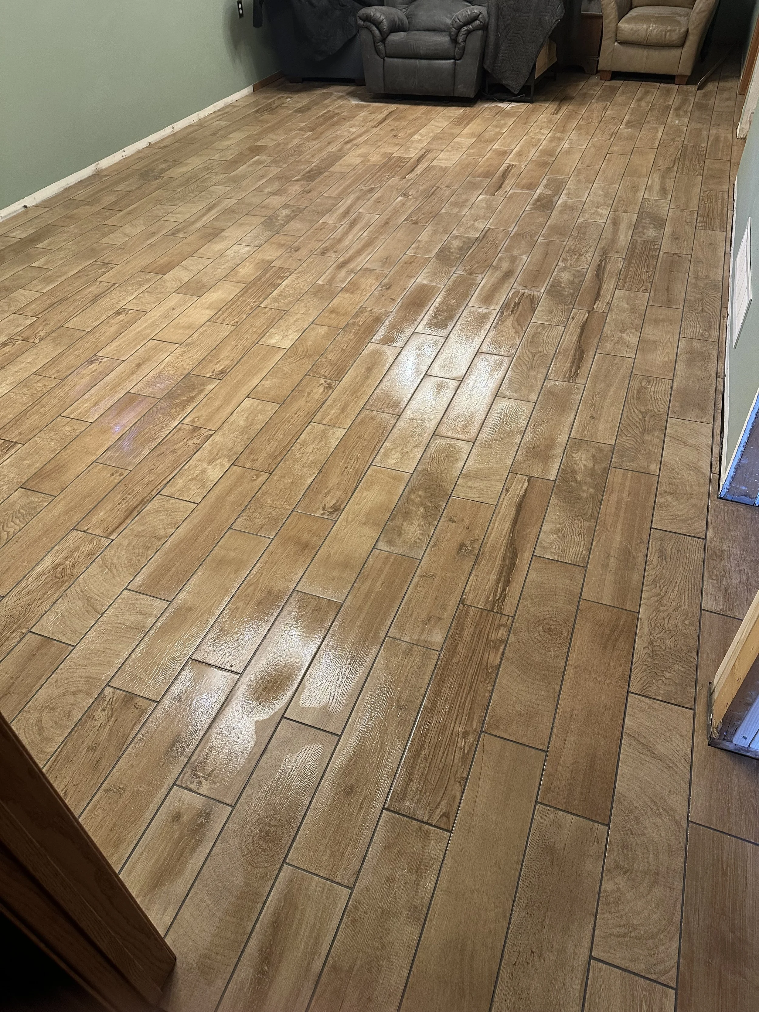 Wooden floor inside a room with a green wall and furniture in the background.
