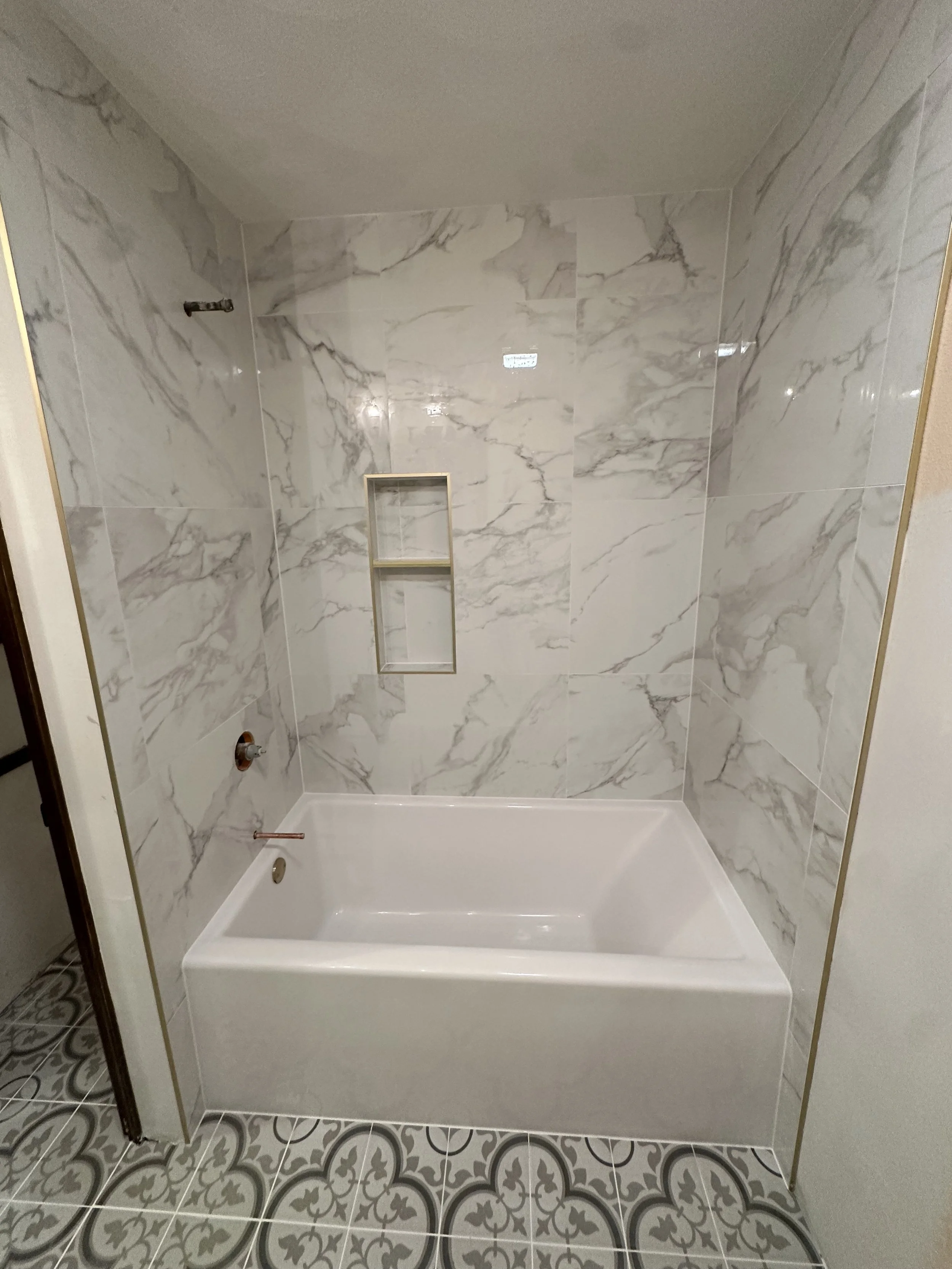 A newly constructed shower with marble wall tiles and patterned floor tiles.