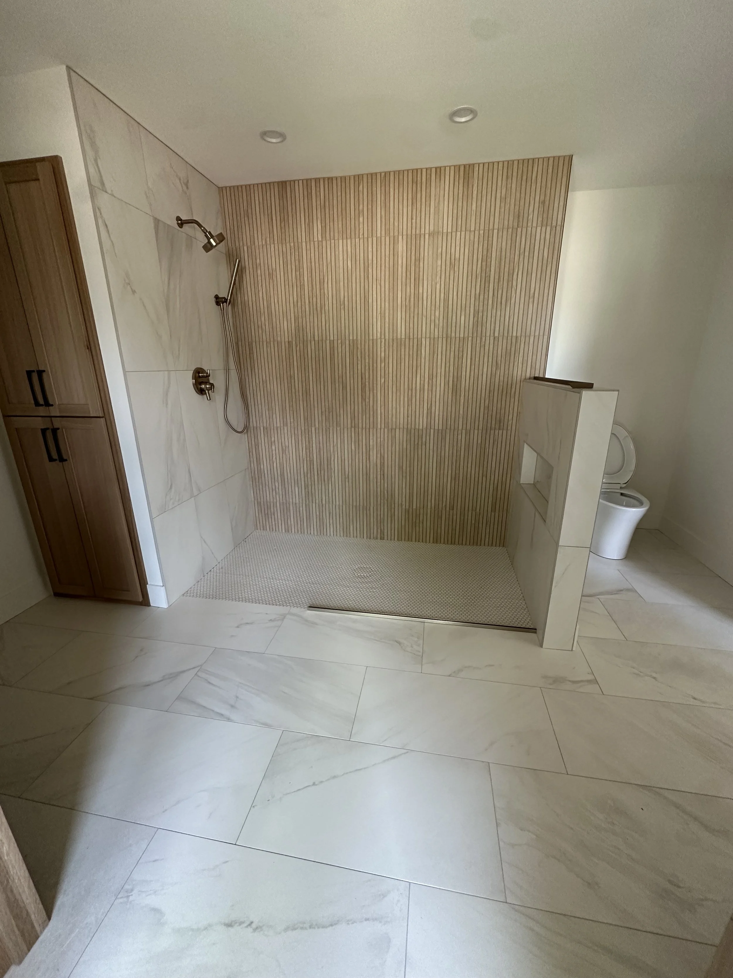 Modern bathroom with a walk-in shower, white marble tiles, a wooden cabinet, and a toilet in a corner.