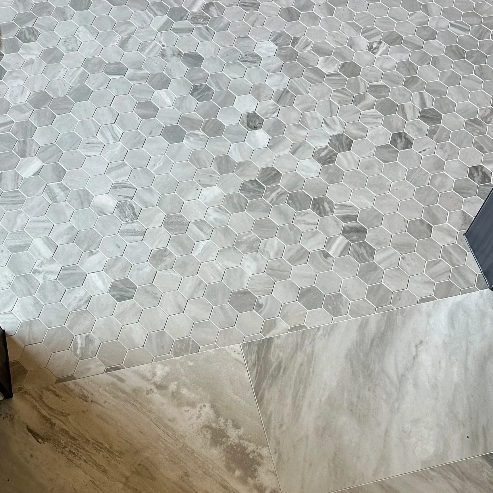 A tiled bathroom wall with three different types of tiles: hexagonal marble tiles at the top, rectangular marble tiles in the middle, and large square marble tiles at the bottom.