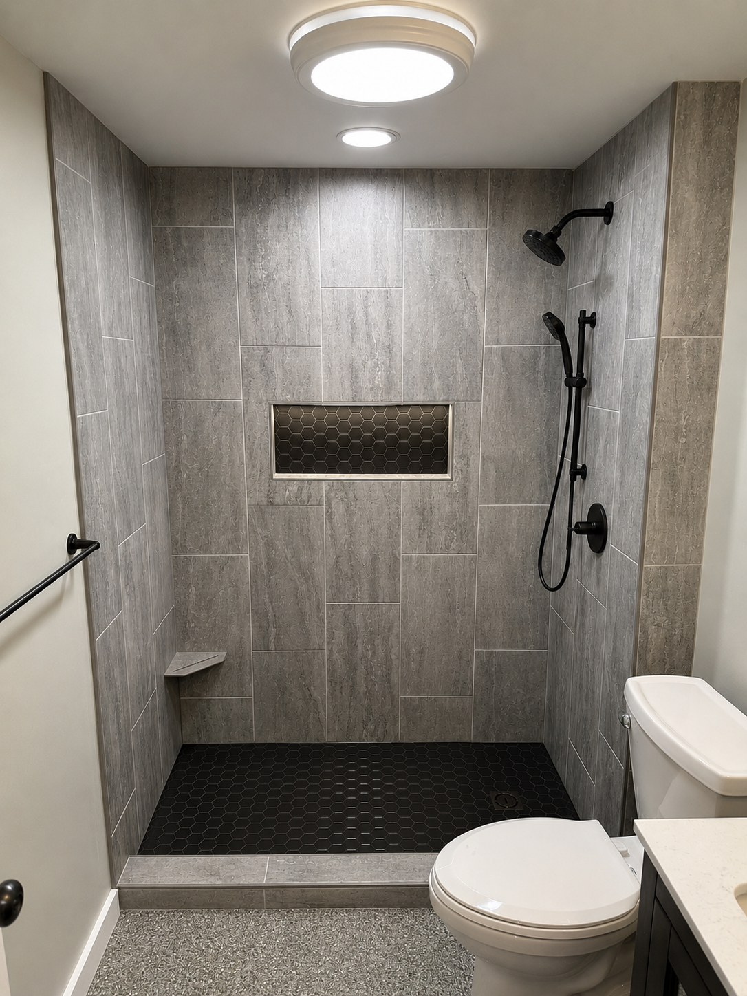 Bathroom with gray tiled walk-in shower, black fixtures, a built-in shelf with honeycomb tile, a toilet, and a towel bar.