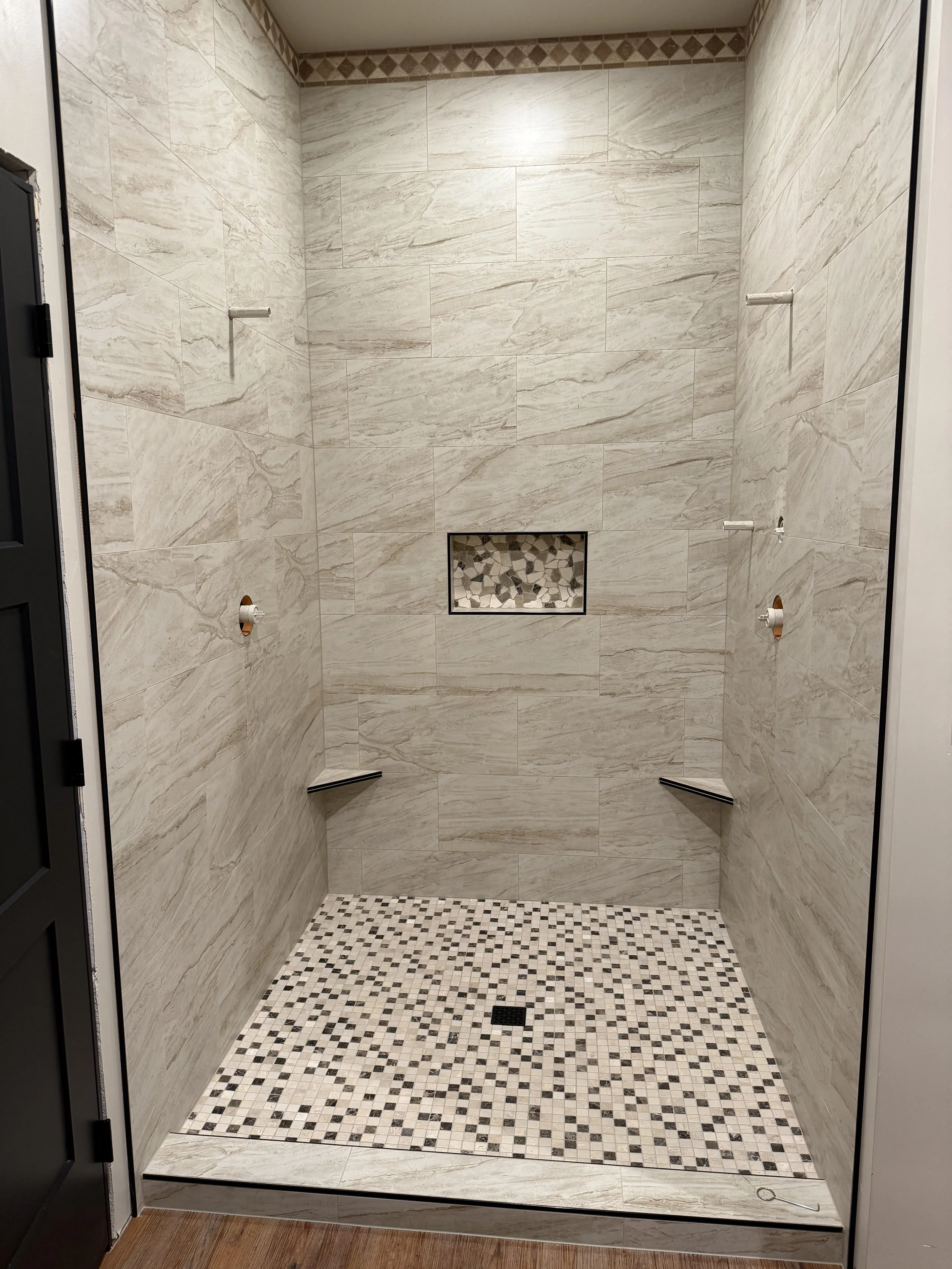 Newly renovated shower with beige marble tiles, mosaic floor pattern, and a built-in niche with pebble tiles.