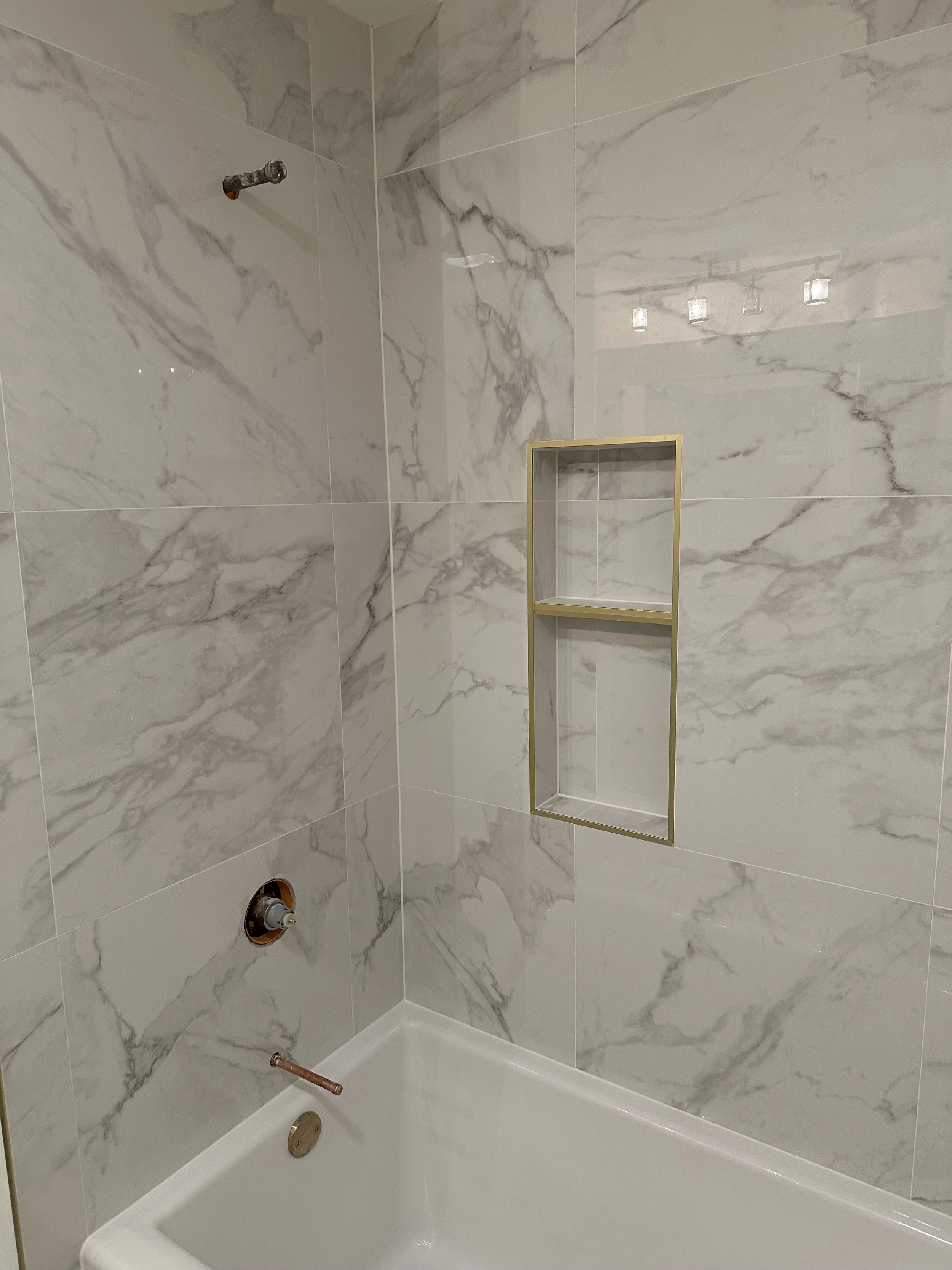 An unfinished marble shower with wall tiles and a built-in niche, plumbing fixtures, and a bathtub.