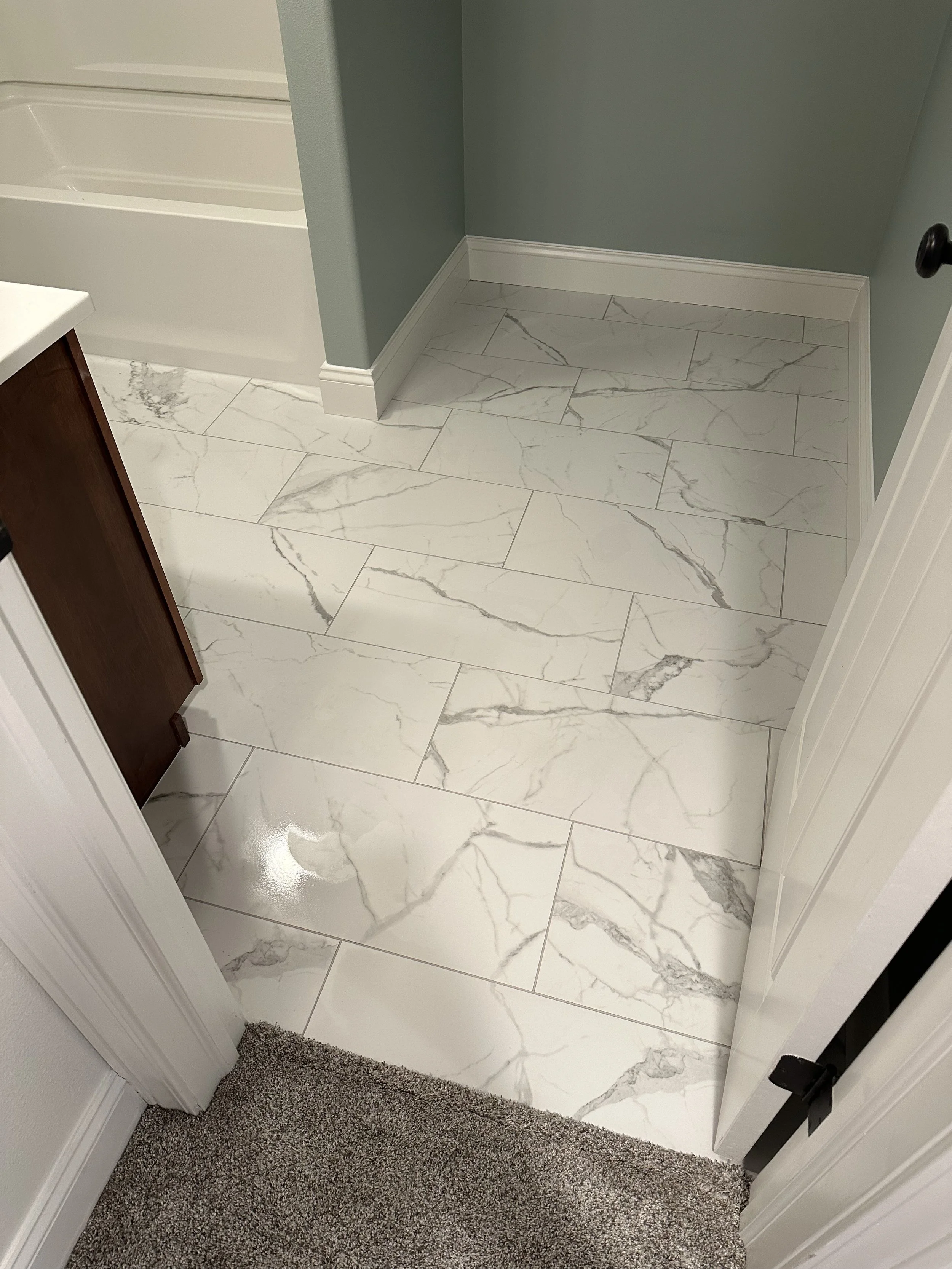 A bathroom floor with hexagonal gray tiles and a central metal drain grate, surrounded by black walls.