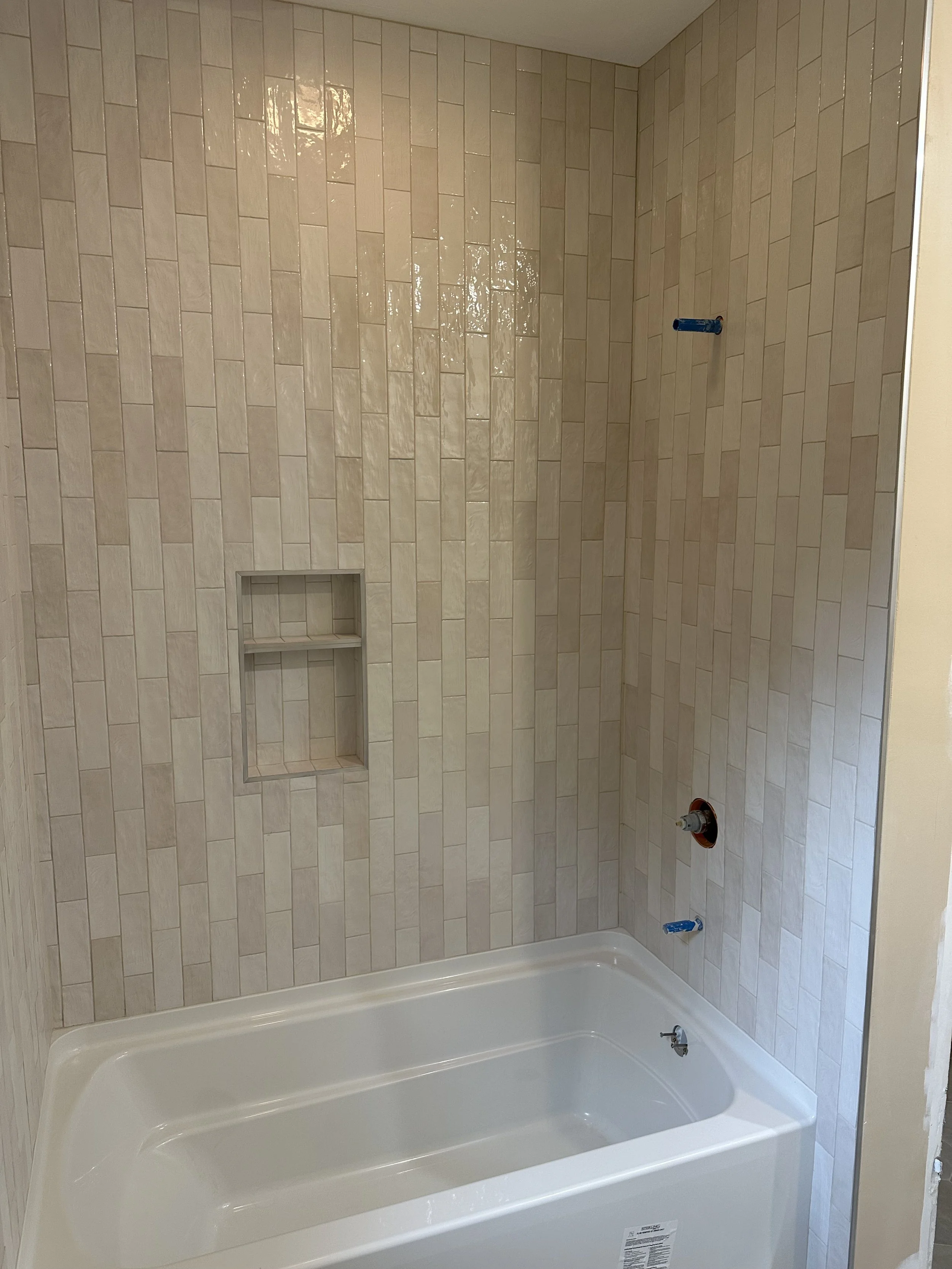 A bathtub in a bathroom with beige tiled walls, an empty built-in recessed shelf, and plumbing fixtures not yet installed.