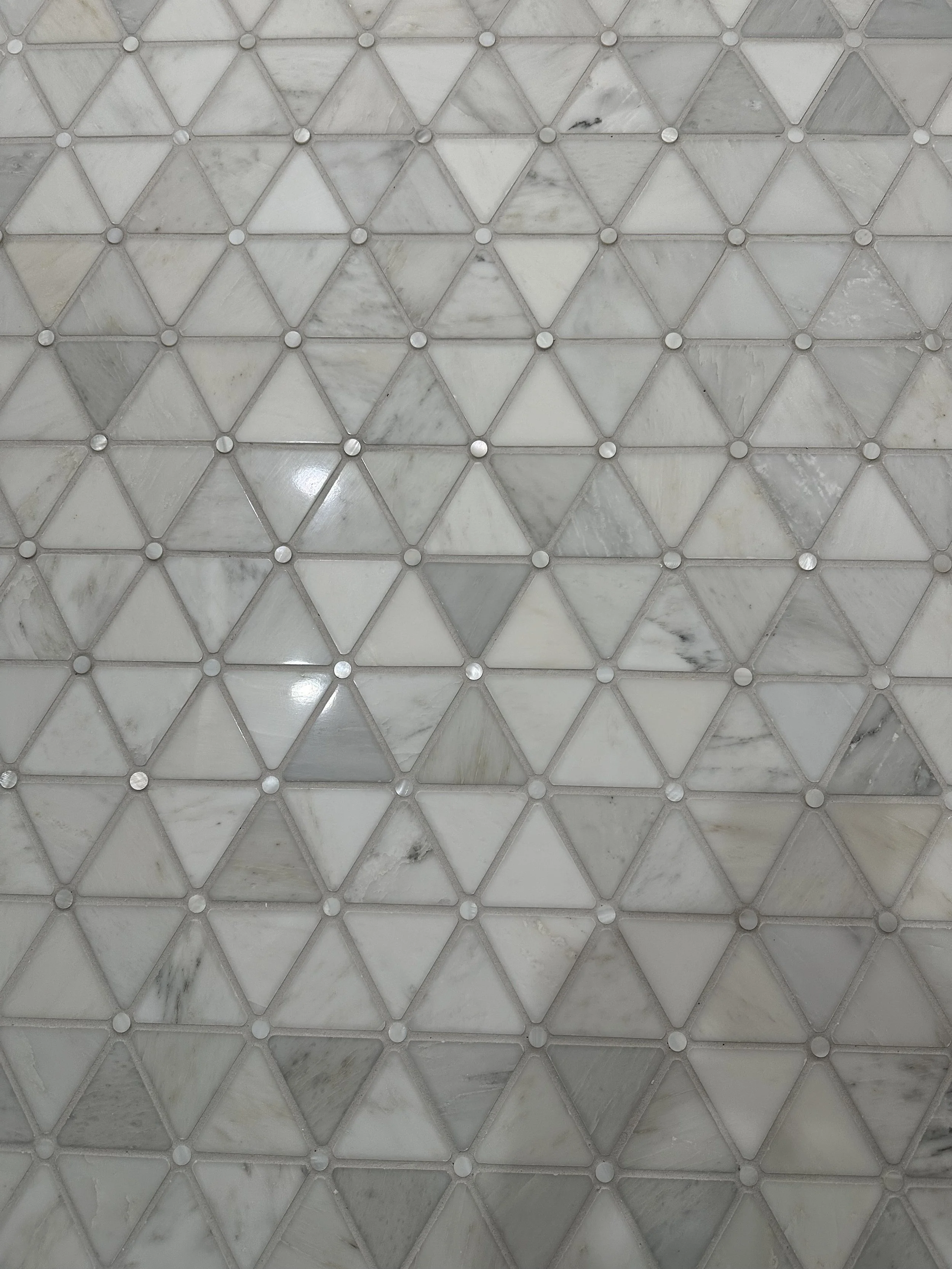 Close-up of a tiled surface with arranged triangular marble tiles and small round metal fasteners.
