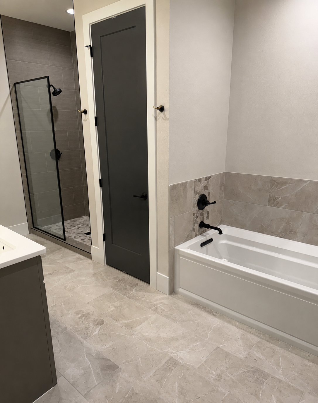 Modern bathroom with a walk-in shower, bathtub, gray door, and neutral tile flooring and wall accents.