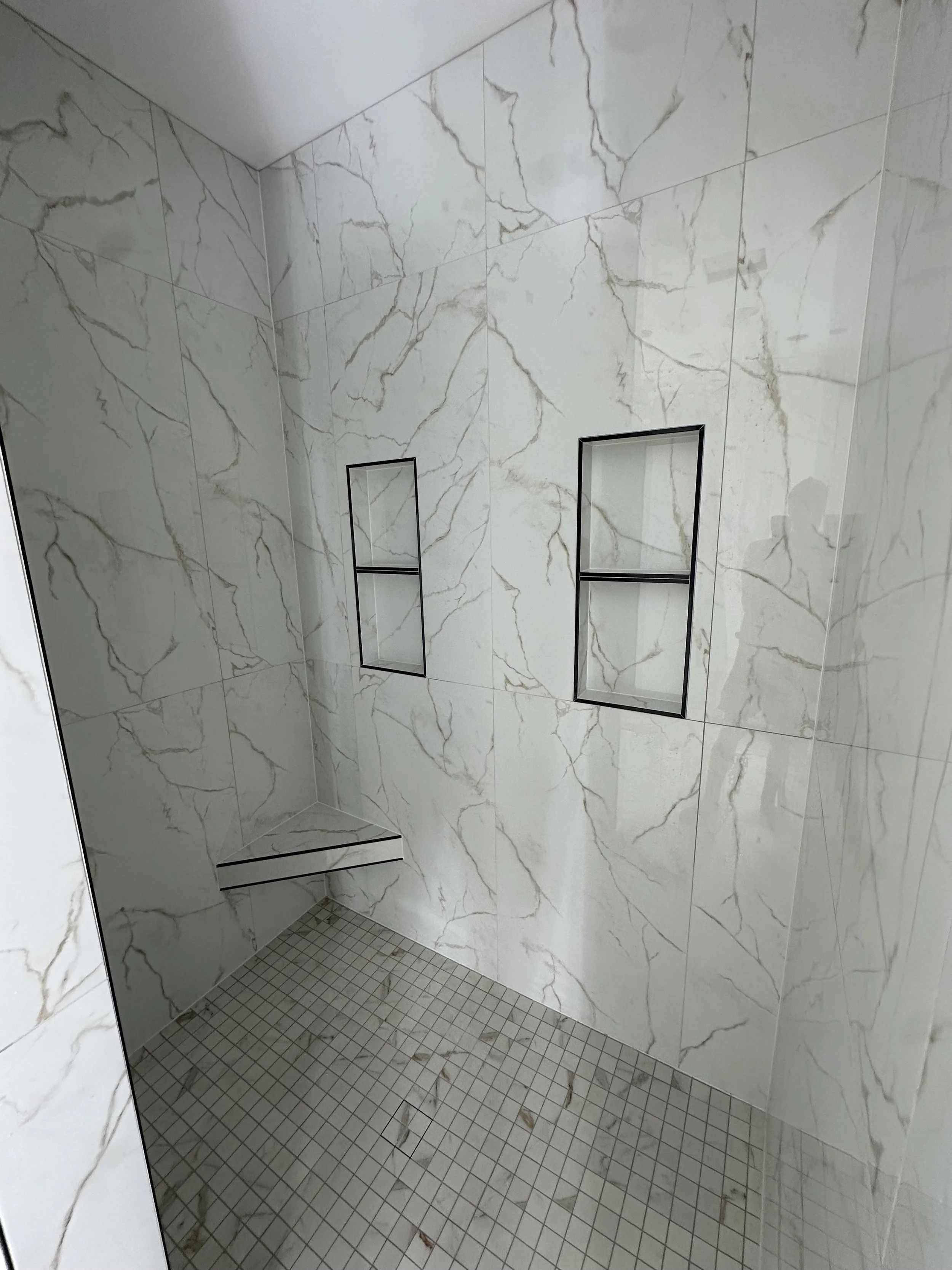Upside-down view of a shower with white marble-patterned tiles, two recessed shelves, and a small tiled floor.