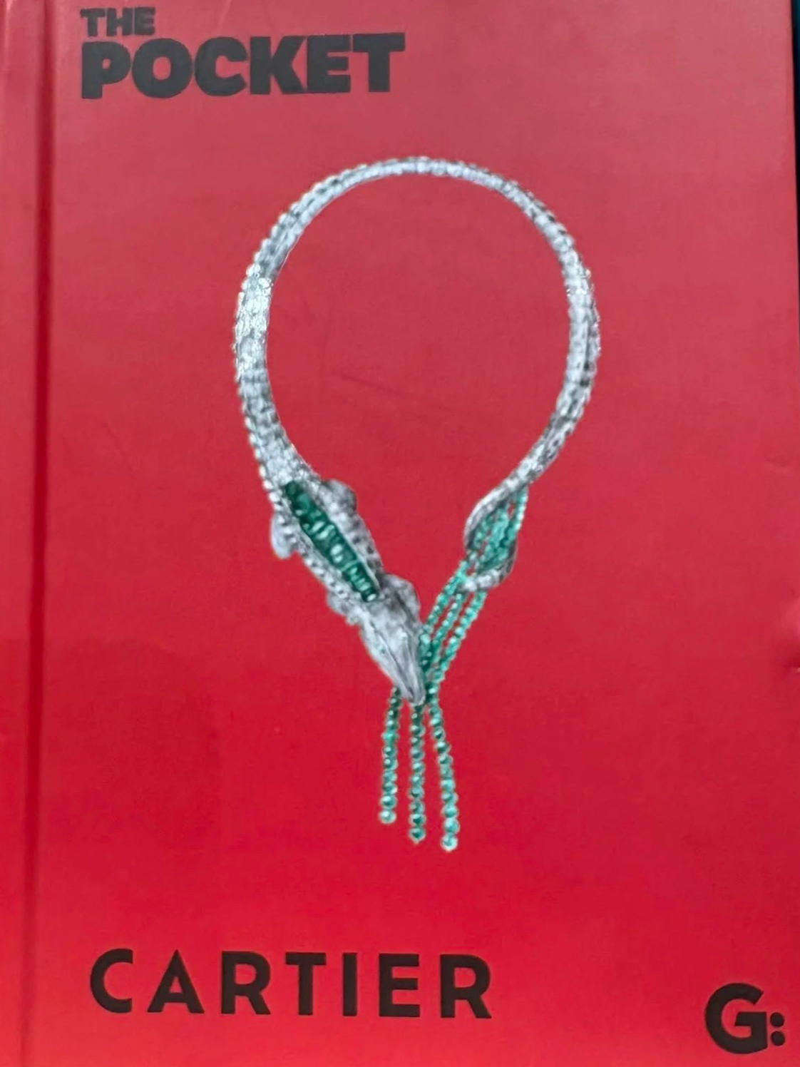Libro rojo titulado 'The Pocket Cartier' con una imagen de un collar de diamantes y esmeraldas