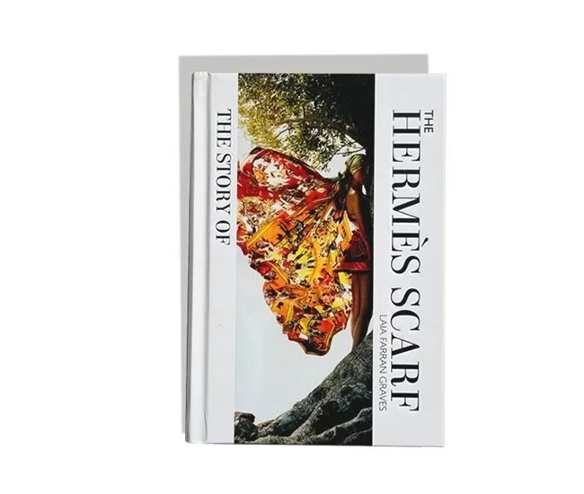 Libro titulado 'The Hermés Scarf: The Story of La Fábrica Graves' con una portada que muestra un pañuelo Hermés con un diseño colorido, colgado de un árbol en un entorno natural.