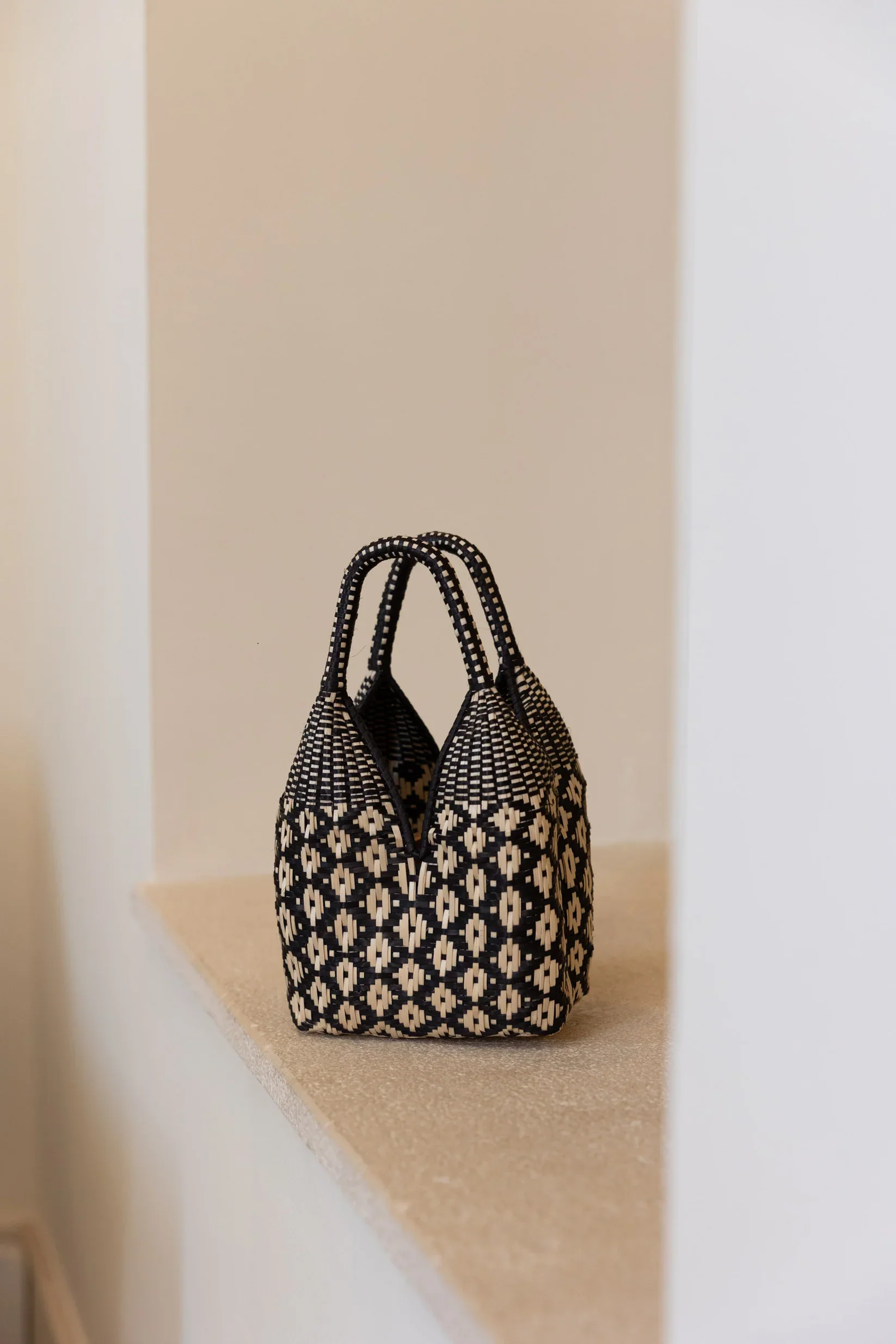 Bolsos hechos con material de cestería en tonos negro, beige y blanco, colocados sobre una repisa de cuarzo en un espacio interior.